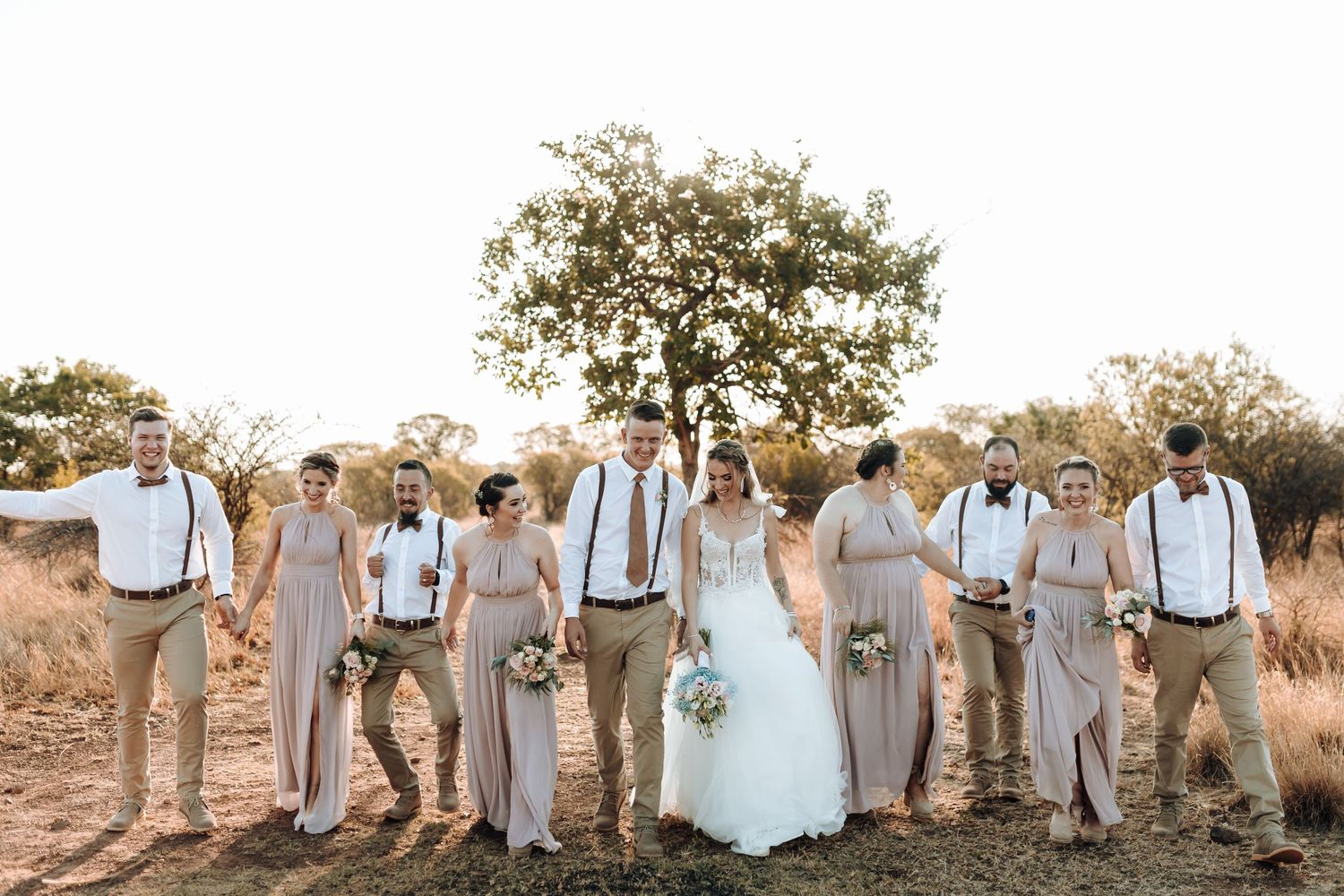 Wedding group in coordinated neutral colors stands against natural landscape backdrop.