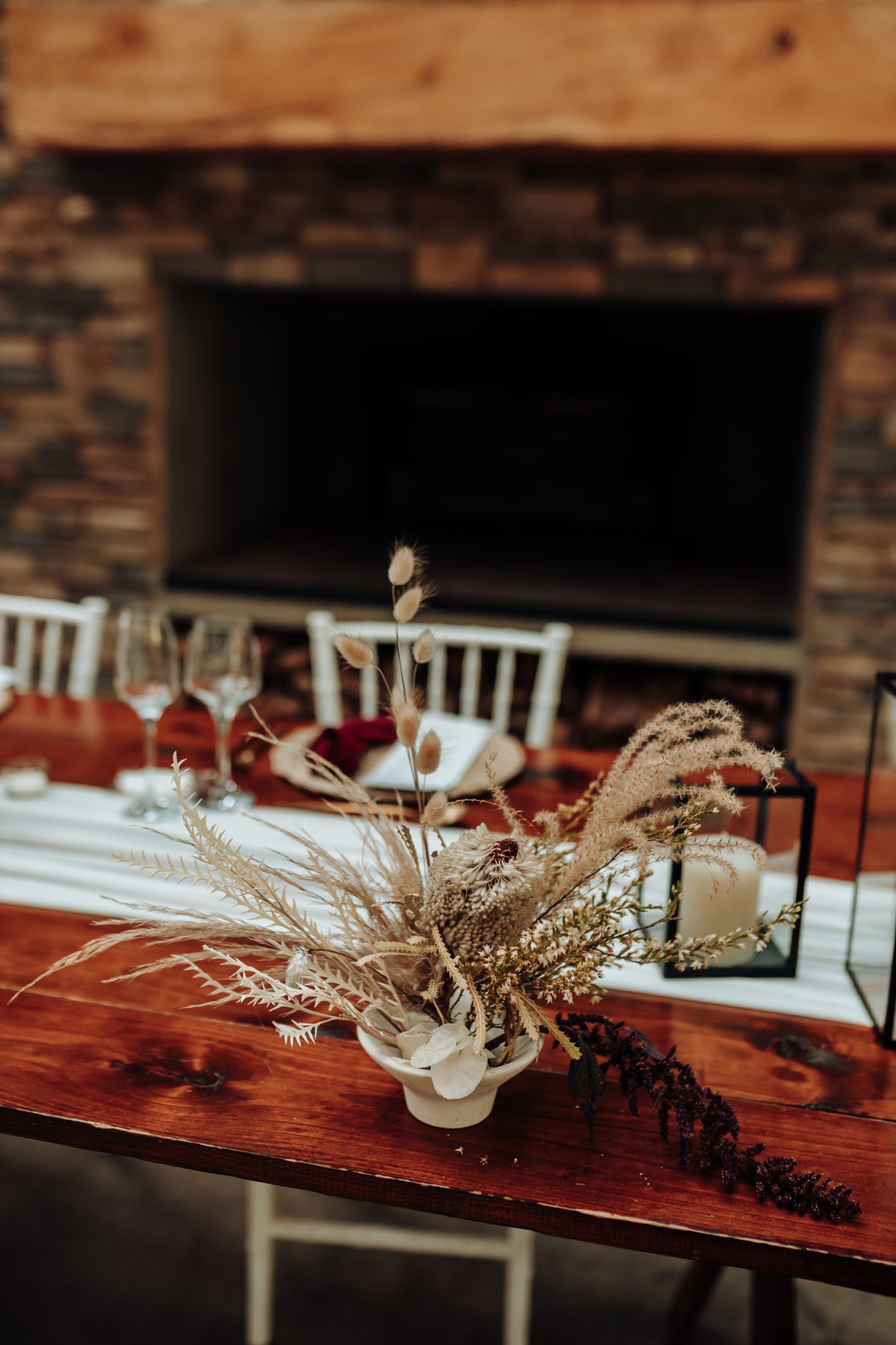 Rustic wedding table centerpiece with dried pampas grass against stone fireplace backdrop.