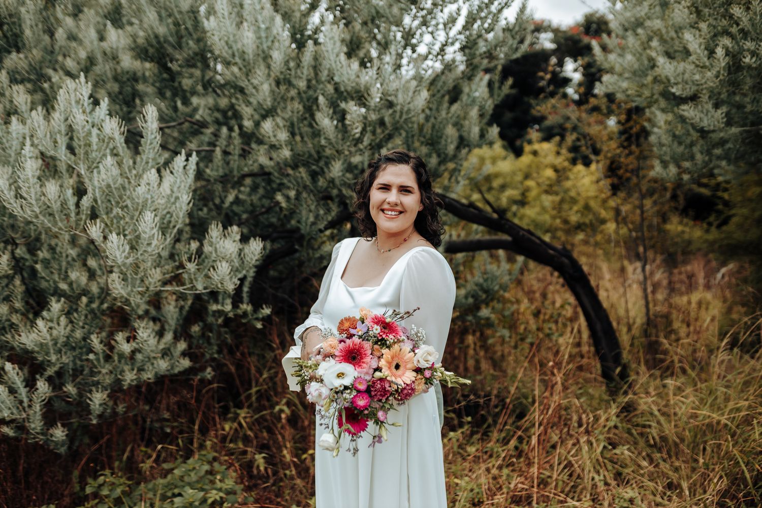 Bright floral bouquet with pink and coral blooms held against a flowing white wedding dress.