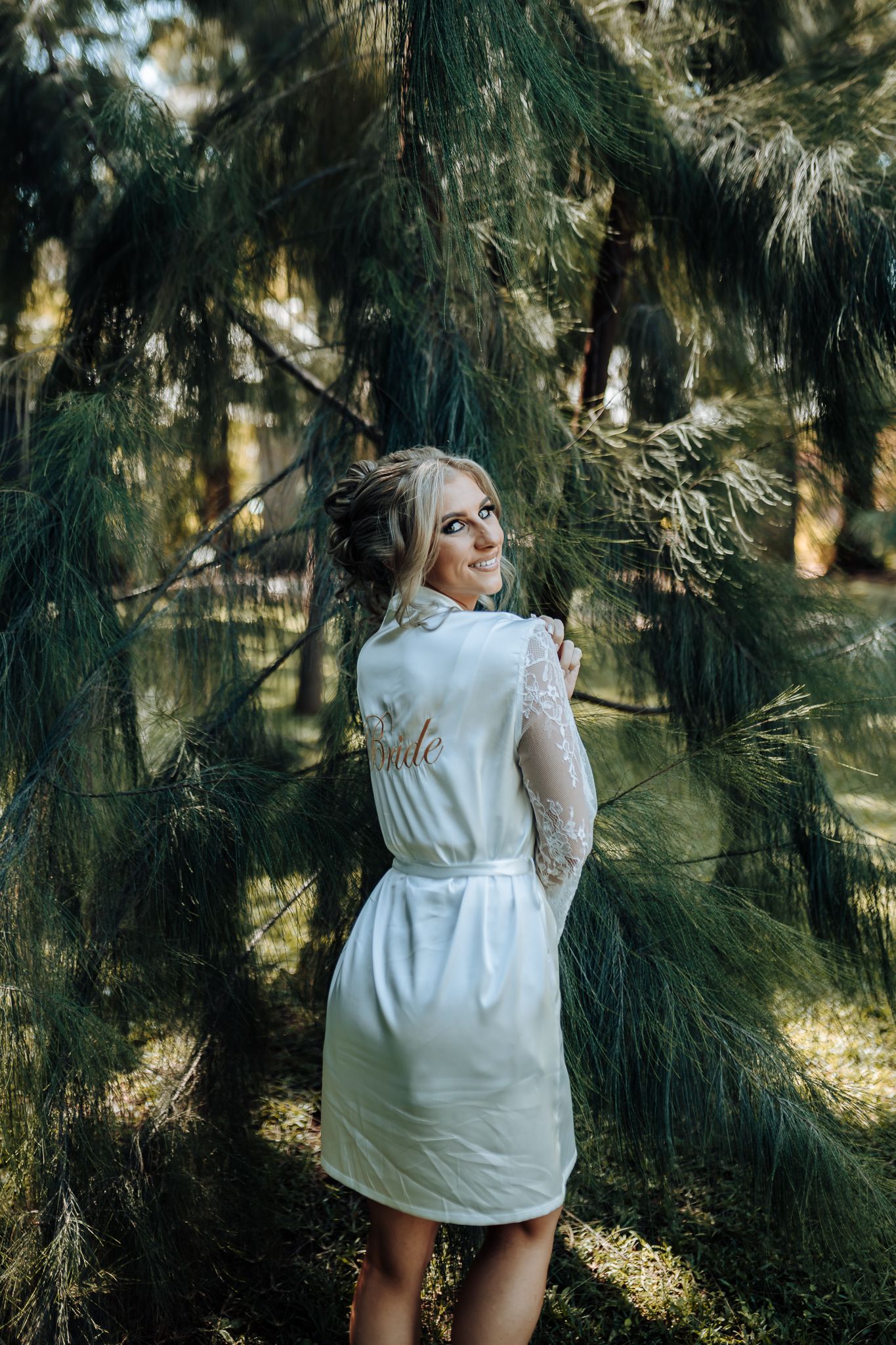 White satin robe captured in a forest setting with pine trees.