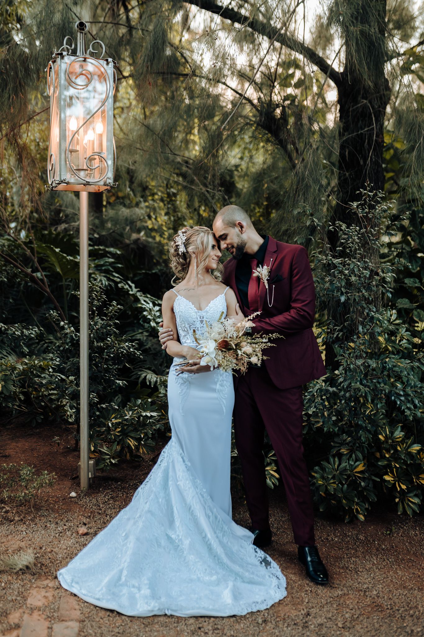 Couple in burgundy suit and light blue wedding dress pose beneath a vintage lantern.