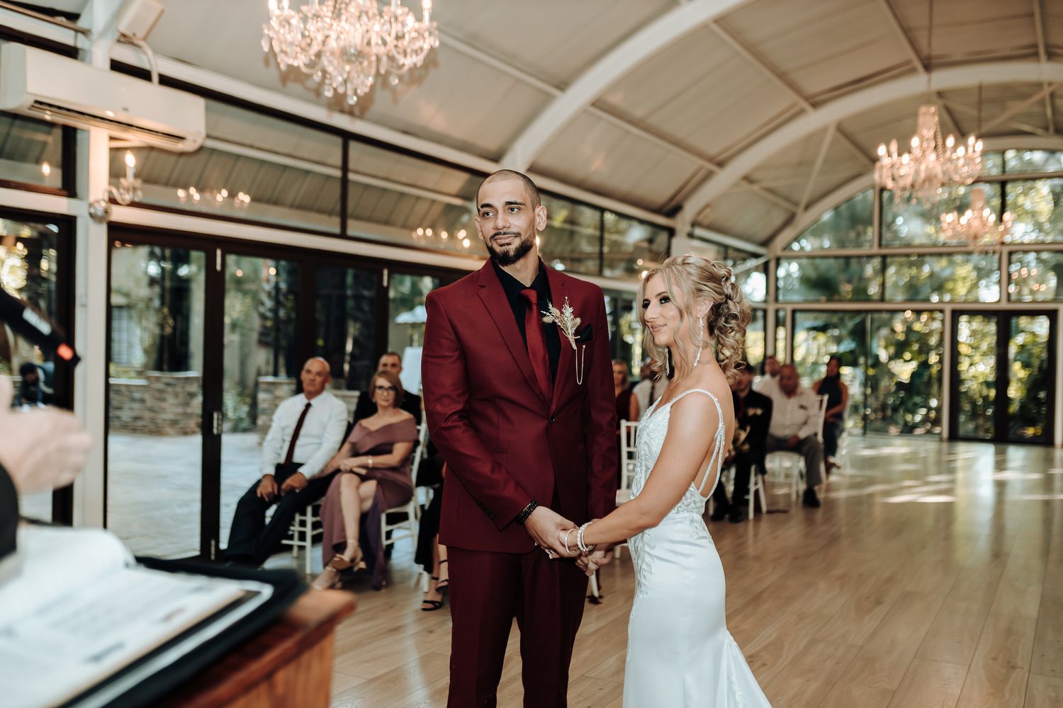Couple shares intimate moment during wedding ceremony in venue with crystal chandeliers.