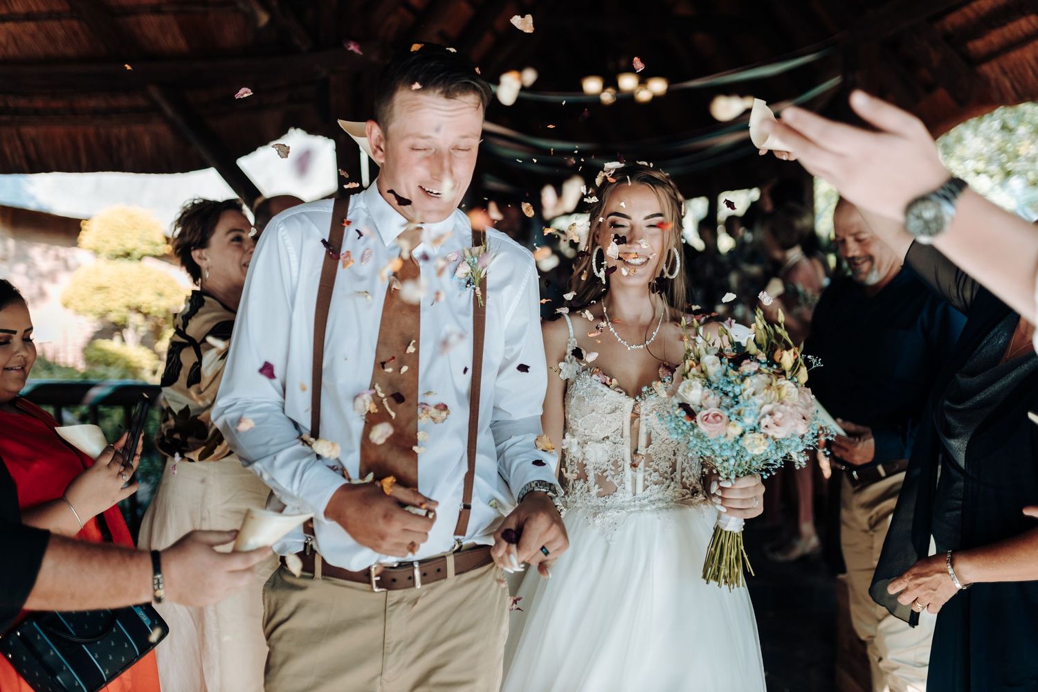 Wedding celebration with couple being showered in confetti under rustic wooden pavilion.