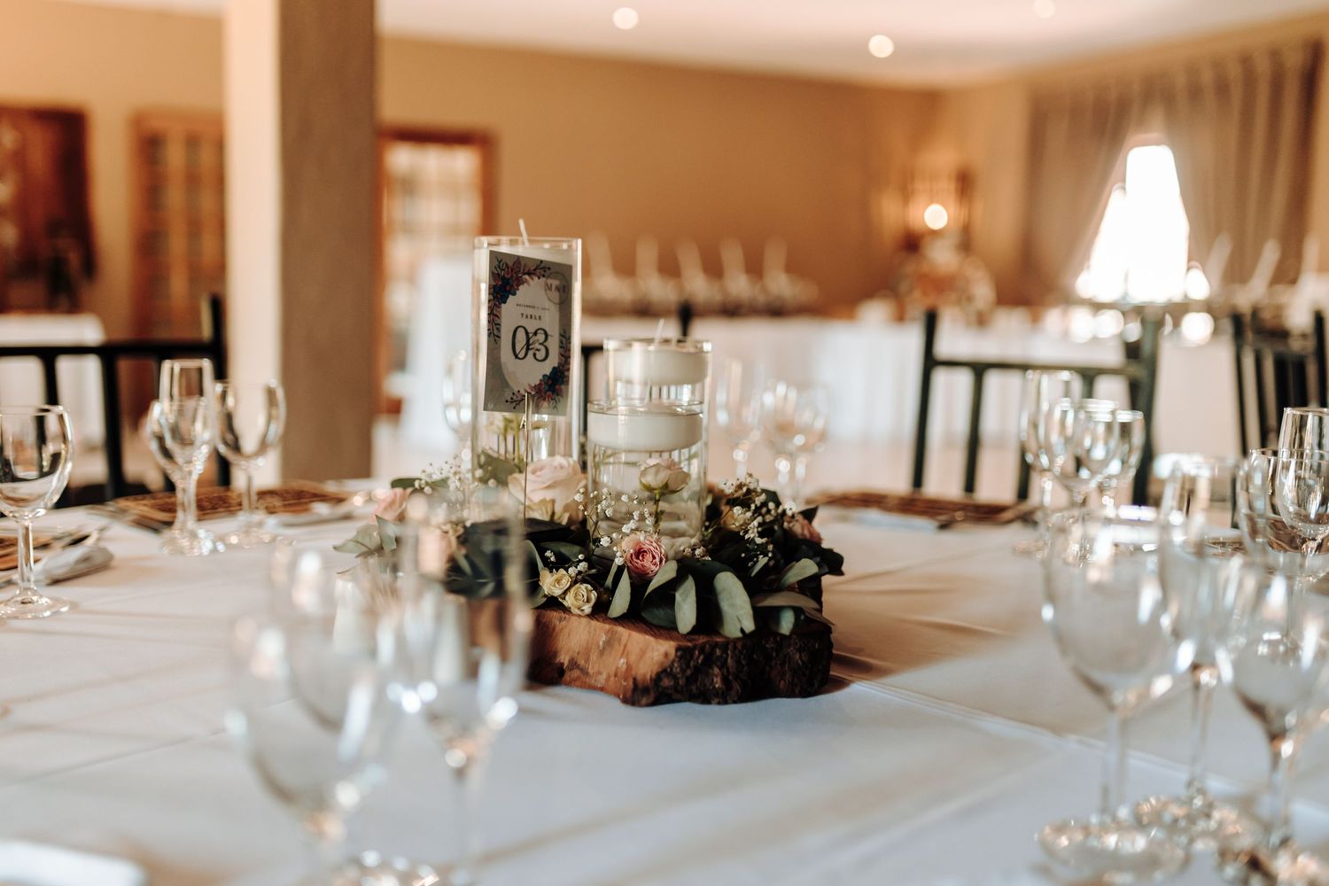 Elegant wedding reception table setting with wine glasses and rustic centerpiece.
