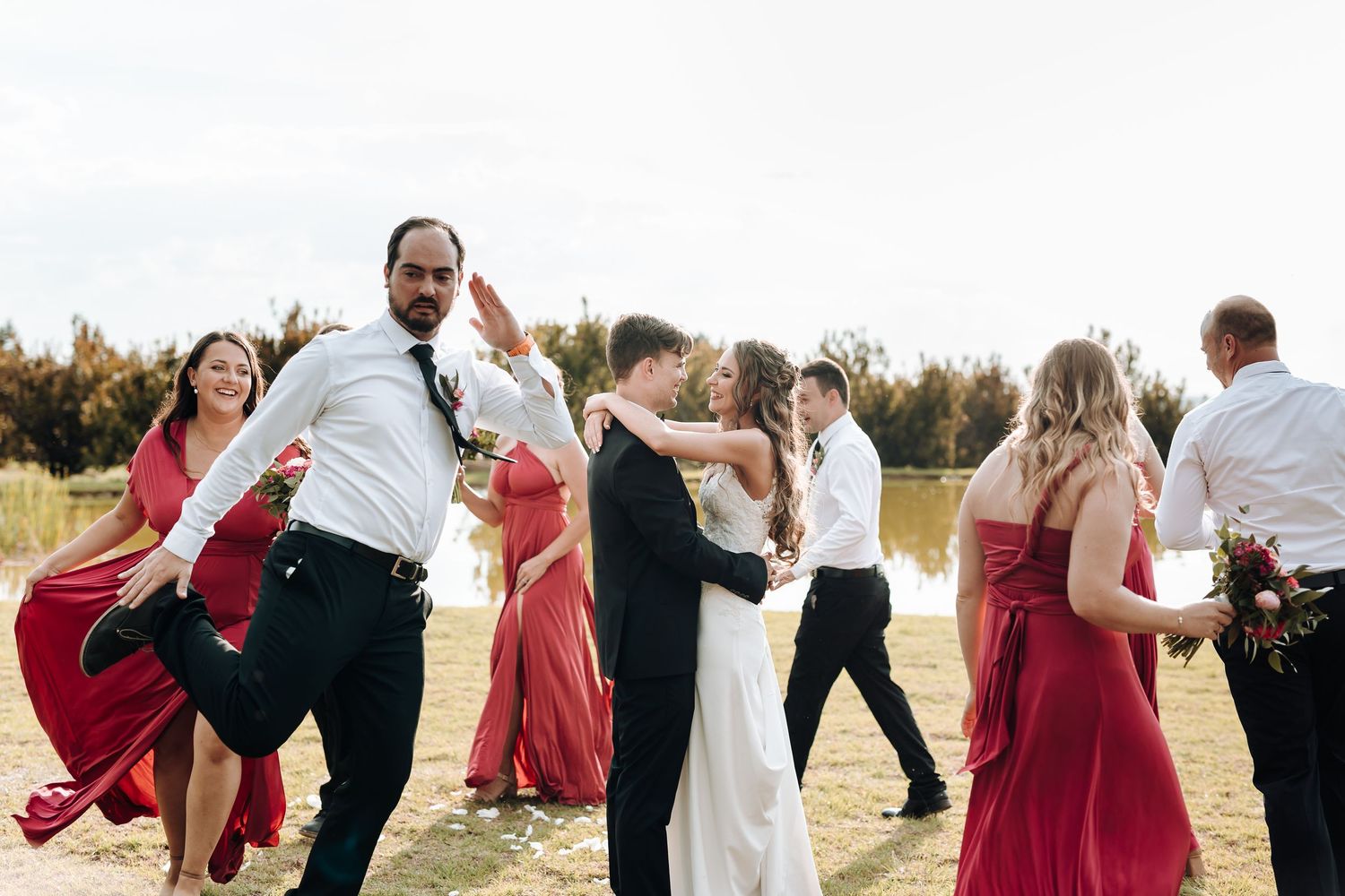 Joyful wedding party dances and celebrates on outdoor grounds.