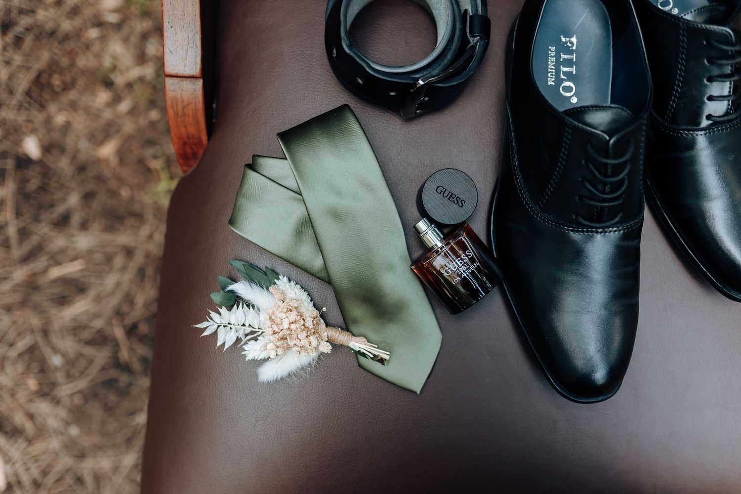Formal black dress shoes with sage green tie and floral boutonniere displayed on brown surface.