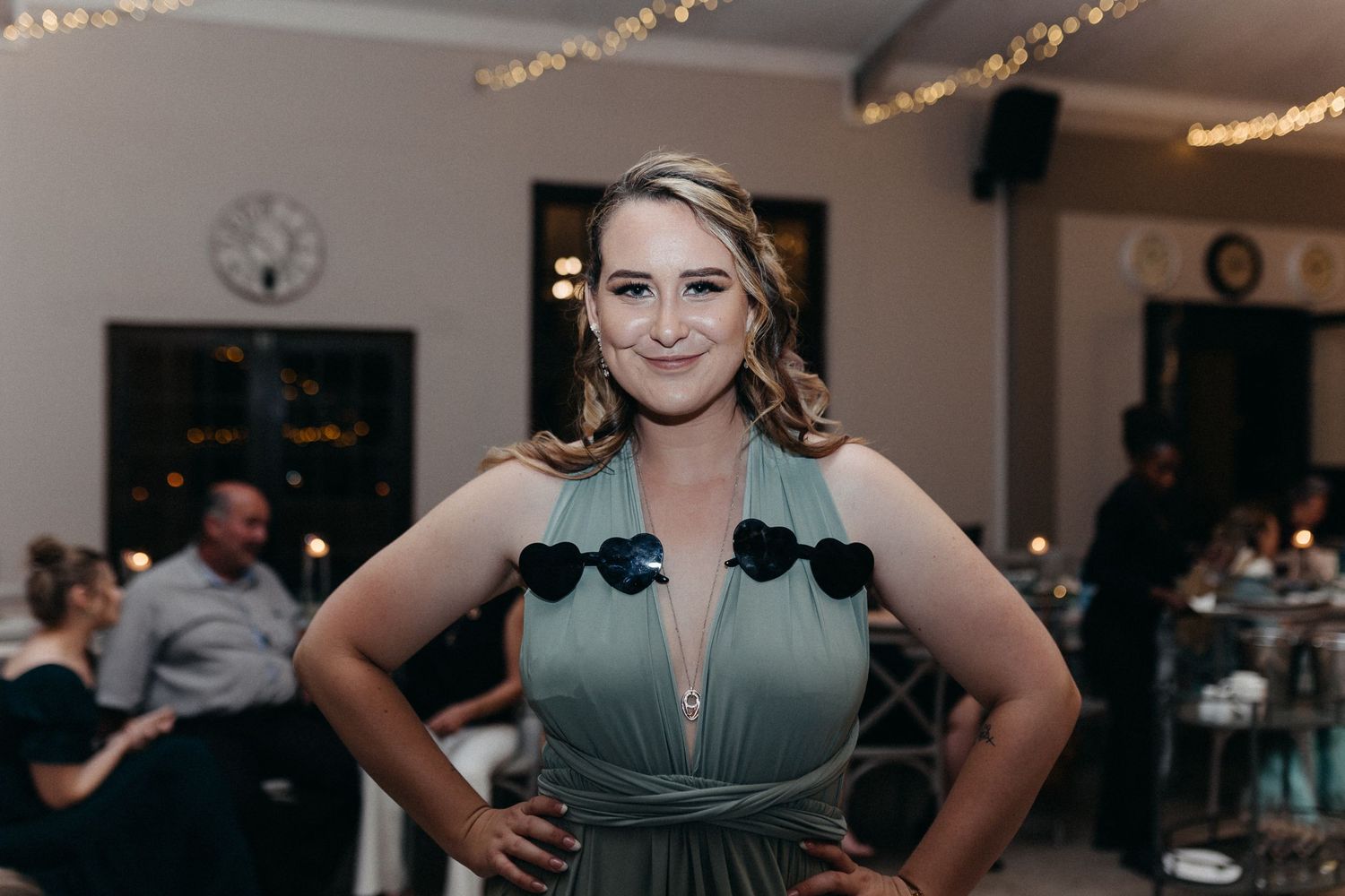 A bridesmaid poses confidently in a sage green dress at a wedding reception.