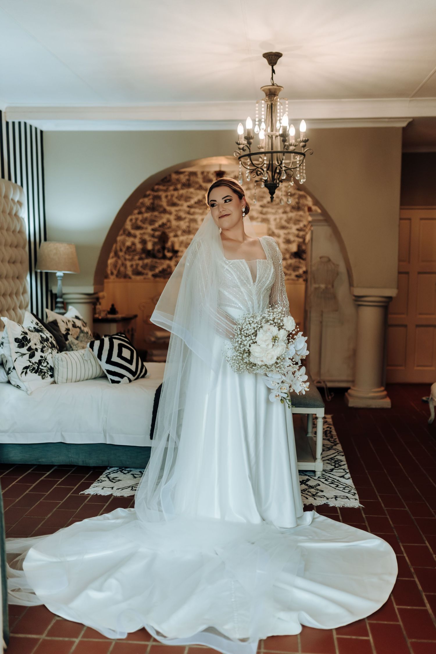 Full-length bridal portrait featuring cathedral train and veil against stone arch backdrop.