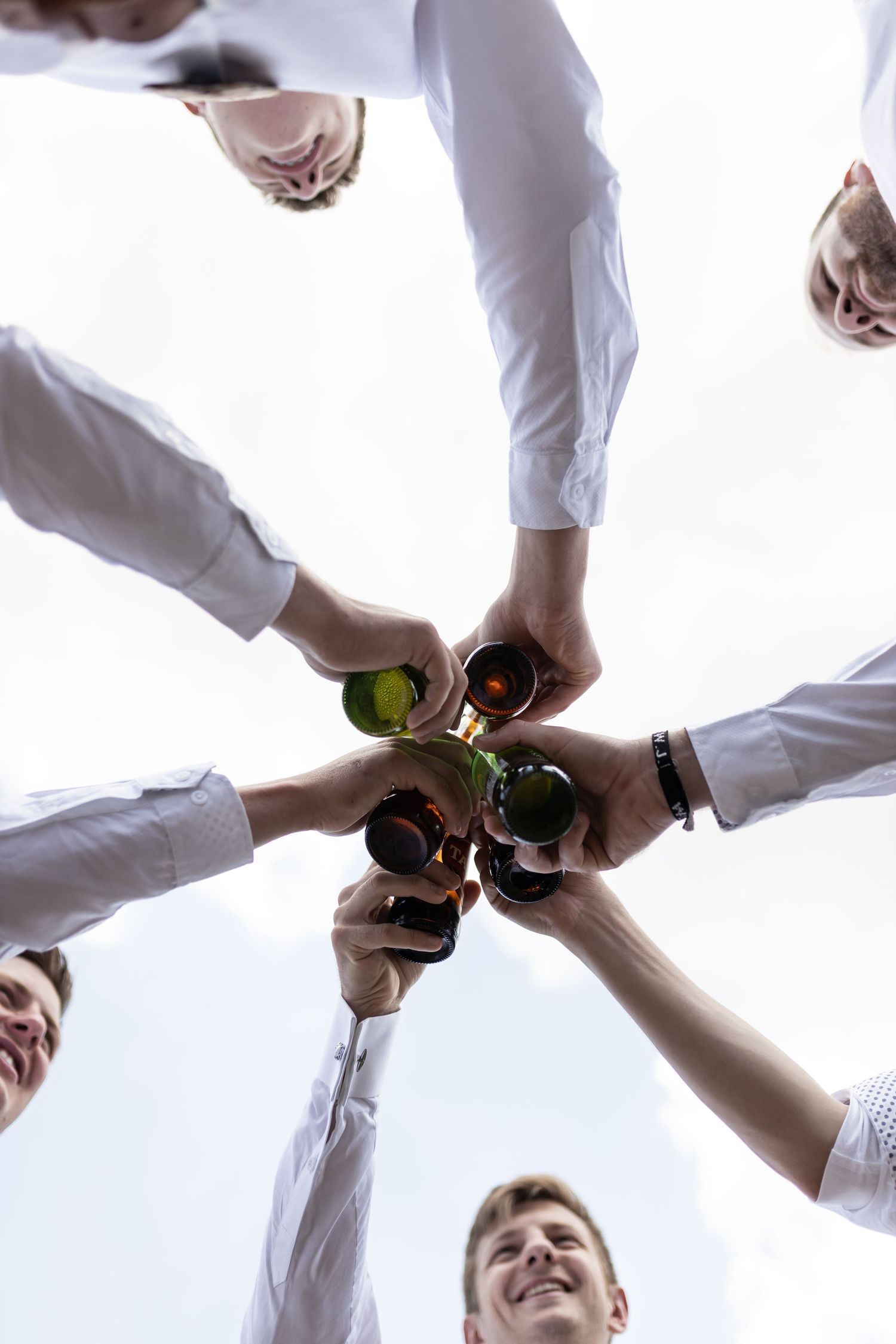 Low angle view of hands joining together in a circle holding bottles for a celebratory toast.