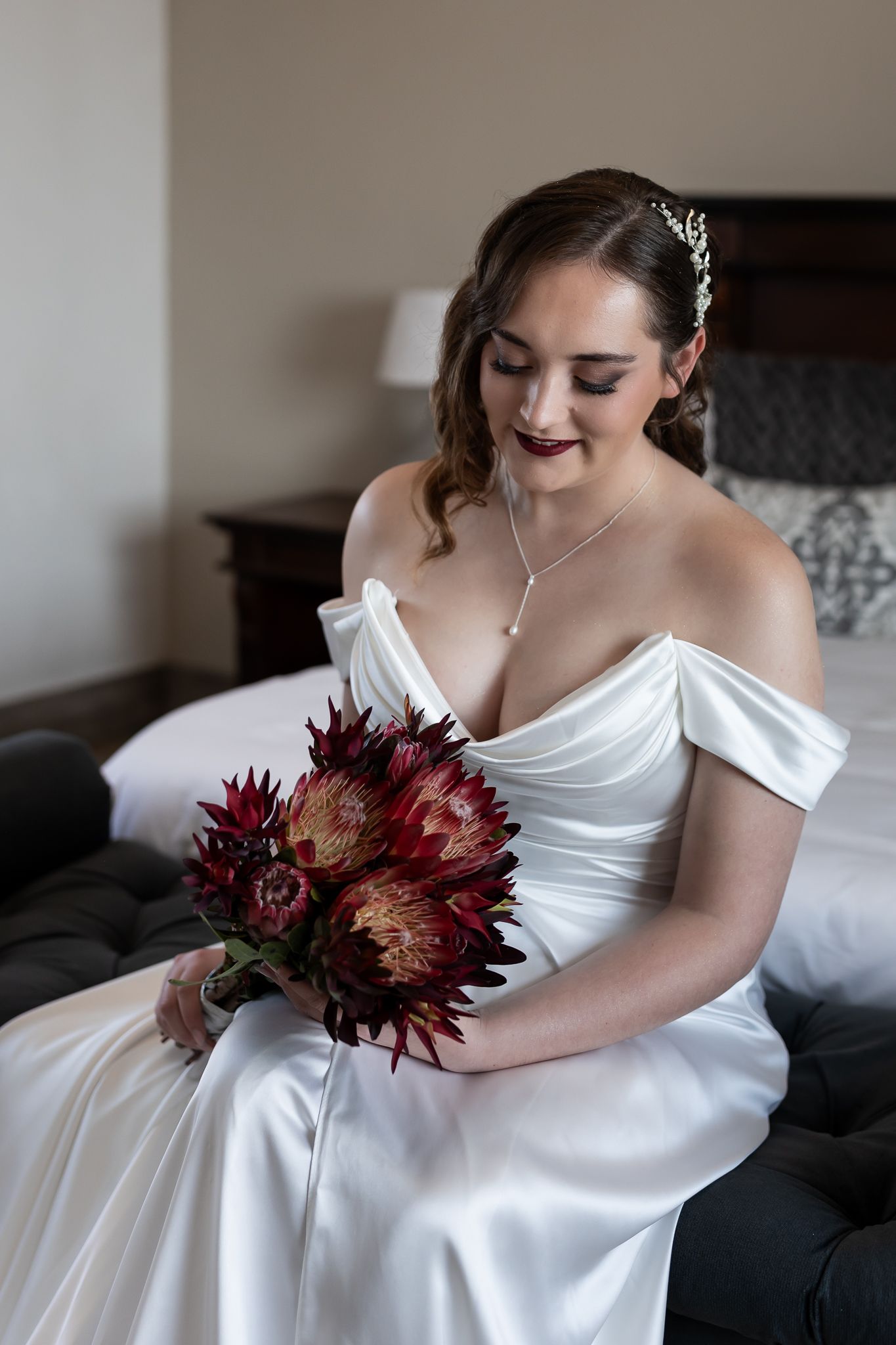 Close-up of bride in white satin dress holding burgundy protea bouquet.