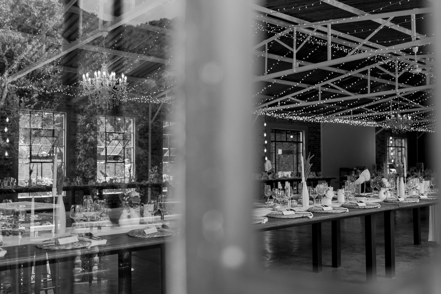Black and white reflection of an elegant wedding reception space with chandeliers and table settings.