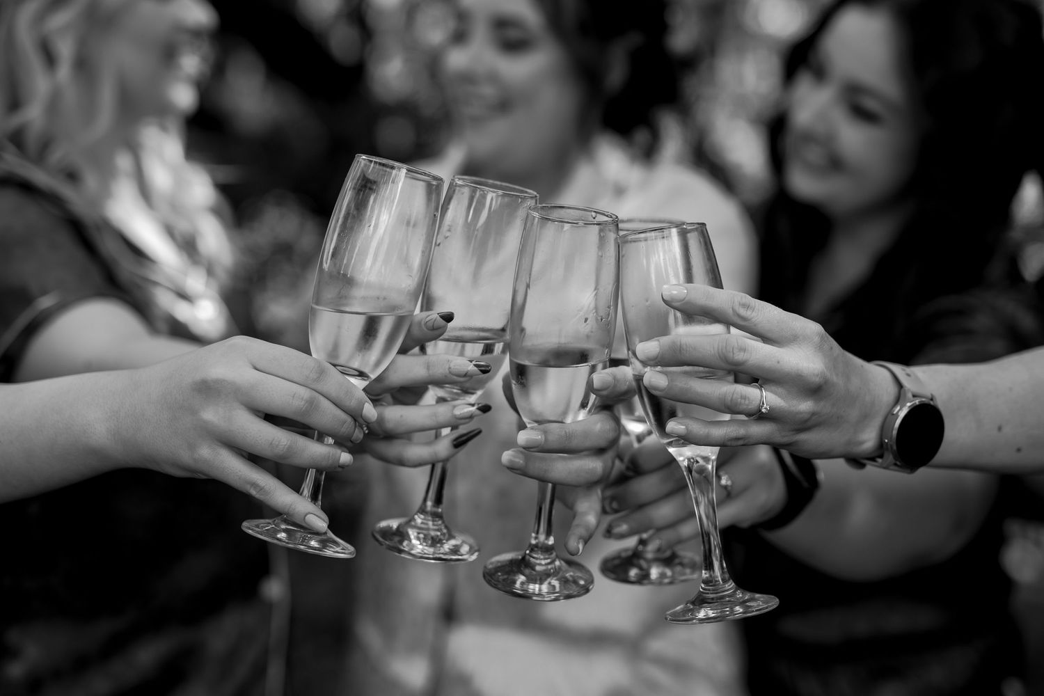 Black and white close-up of champagne glasses clinking together in celebration.