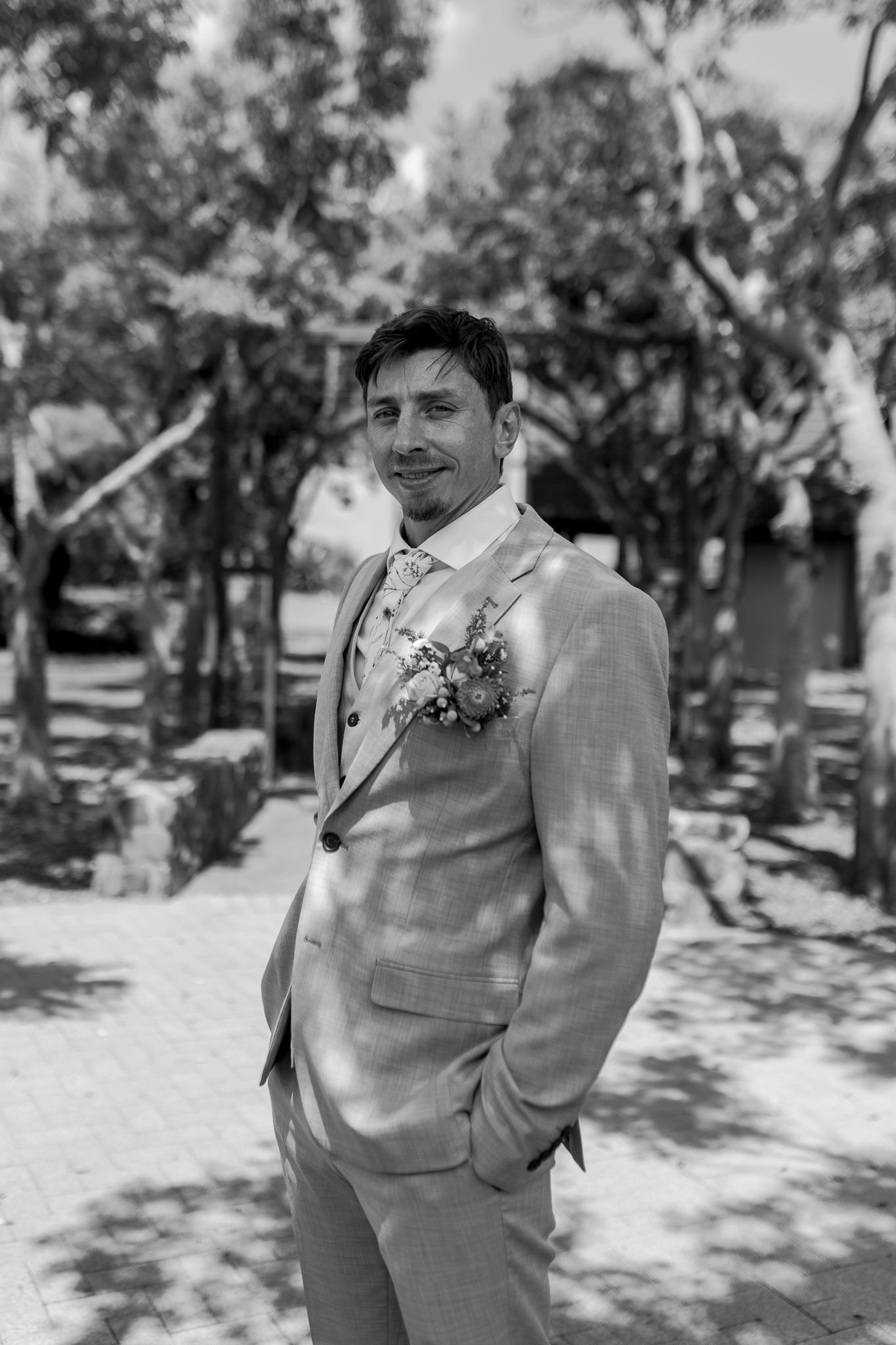 Black and white portrait of groom in light suit outdoors among trees.