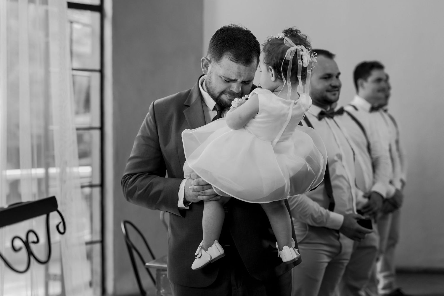 Black and white candid moment from wedding ceremony with formal attire and natural light.