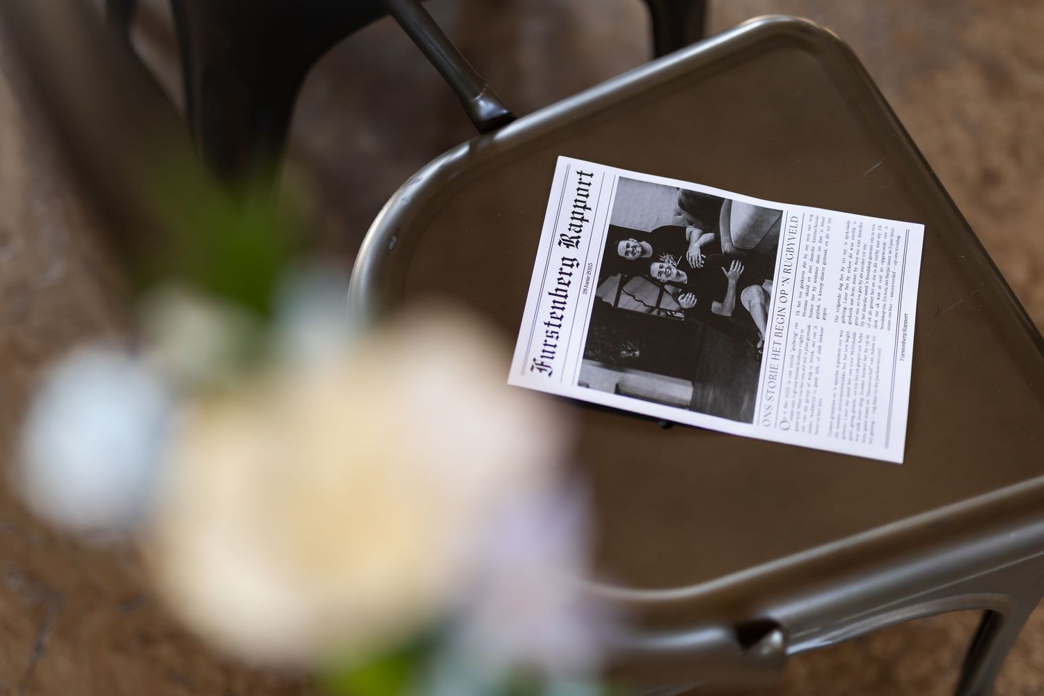 A black and white photo print lies on a metal surface with a blurred white flower in the background.