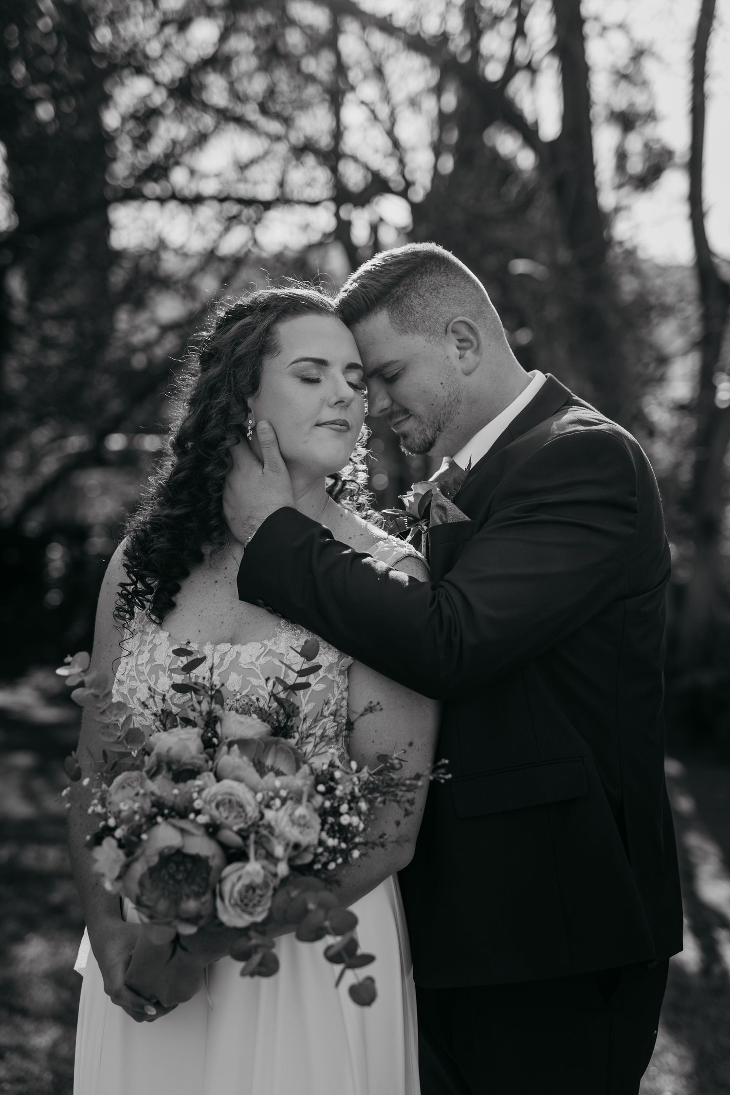 A romantic black and white wedding photo shows a tender moment between newlyweds as the bride holds a floral bouquet.