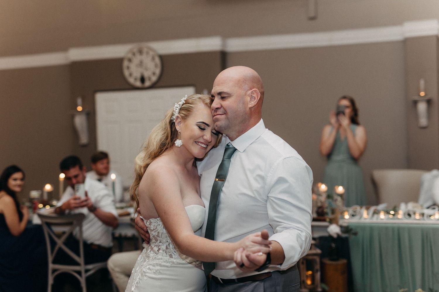 An intimate slow dance at a wedding reception with string lights and decor in the background.