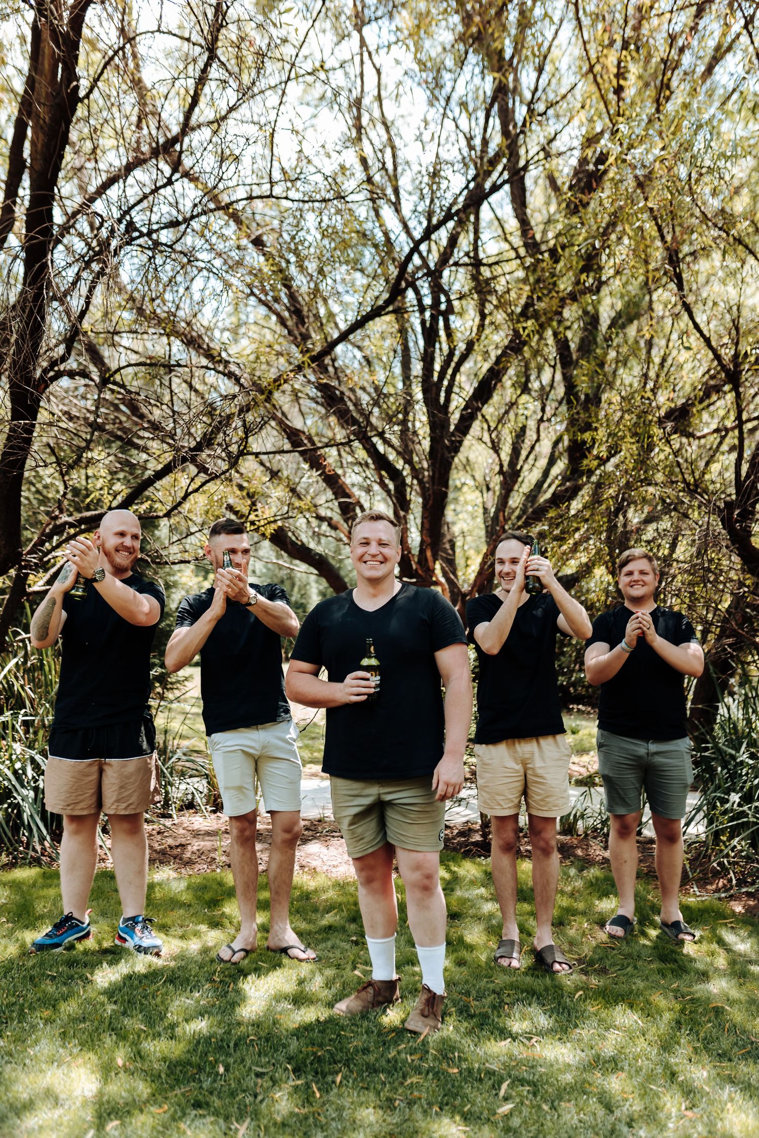 Five friends in coordinated outfits pose playfully in a sunny garden setting.