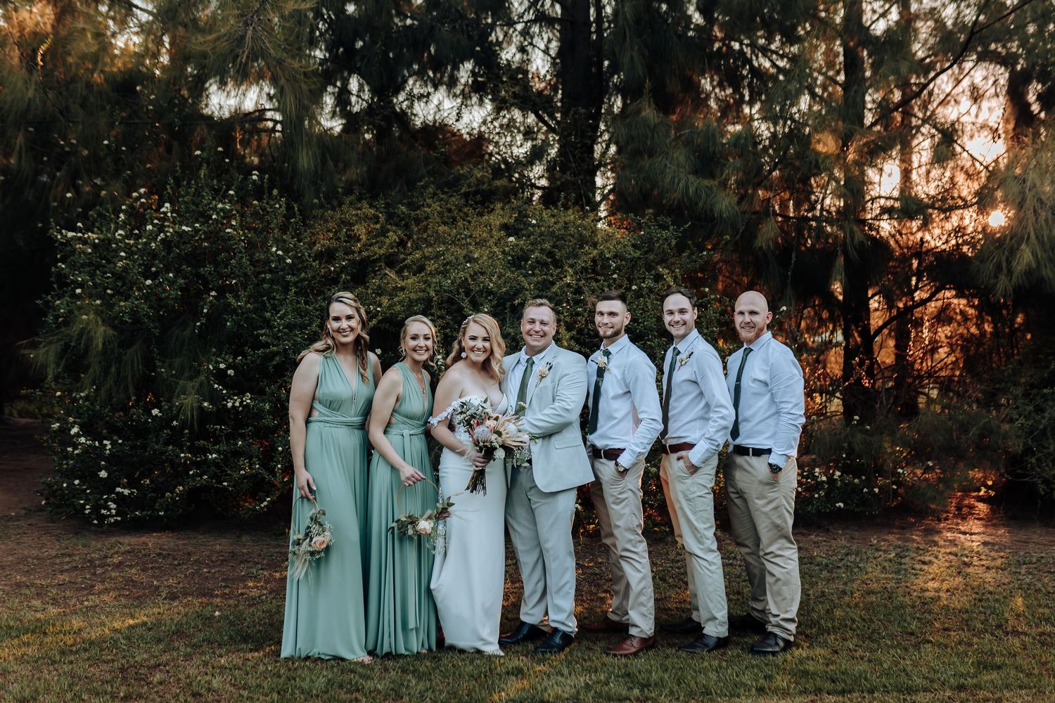 Wedding party in mint green and gray attire posing at sunset.