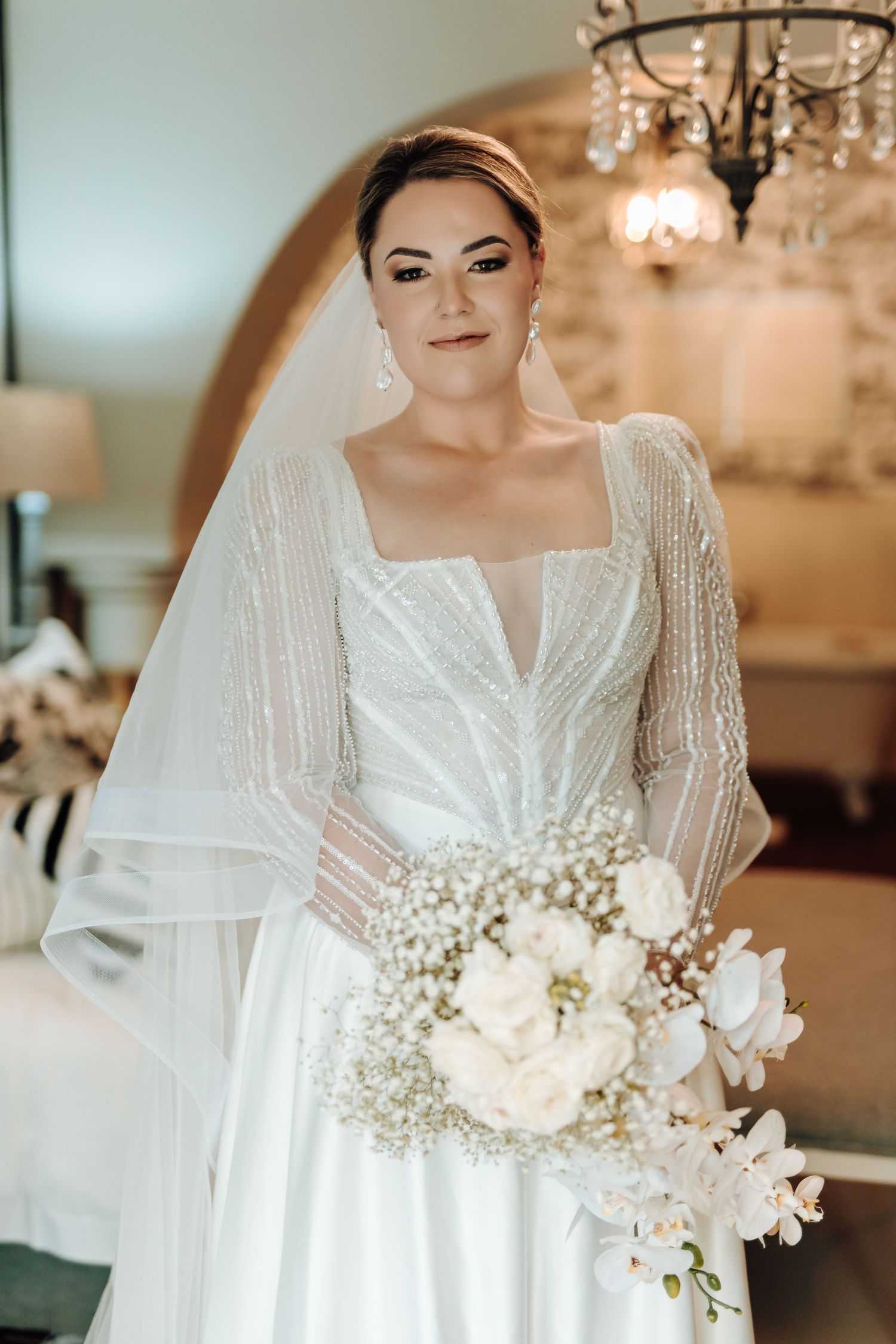 Wedding gown with sheer beaded sleeves and square neckline complemented by white floral and baby's breath bouquet.