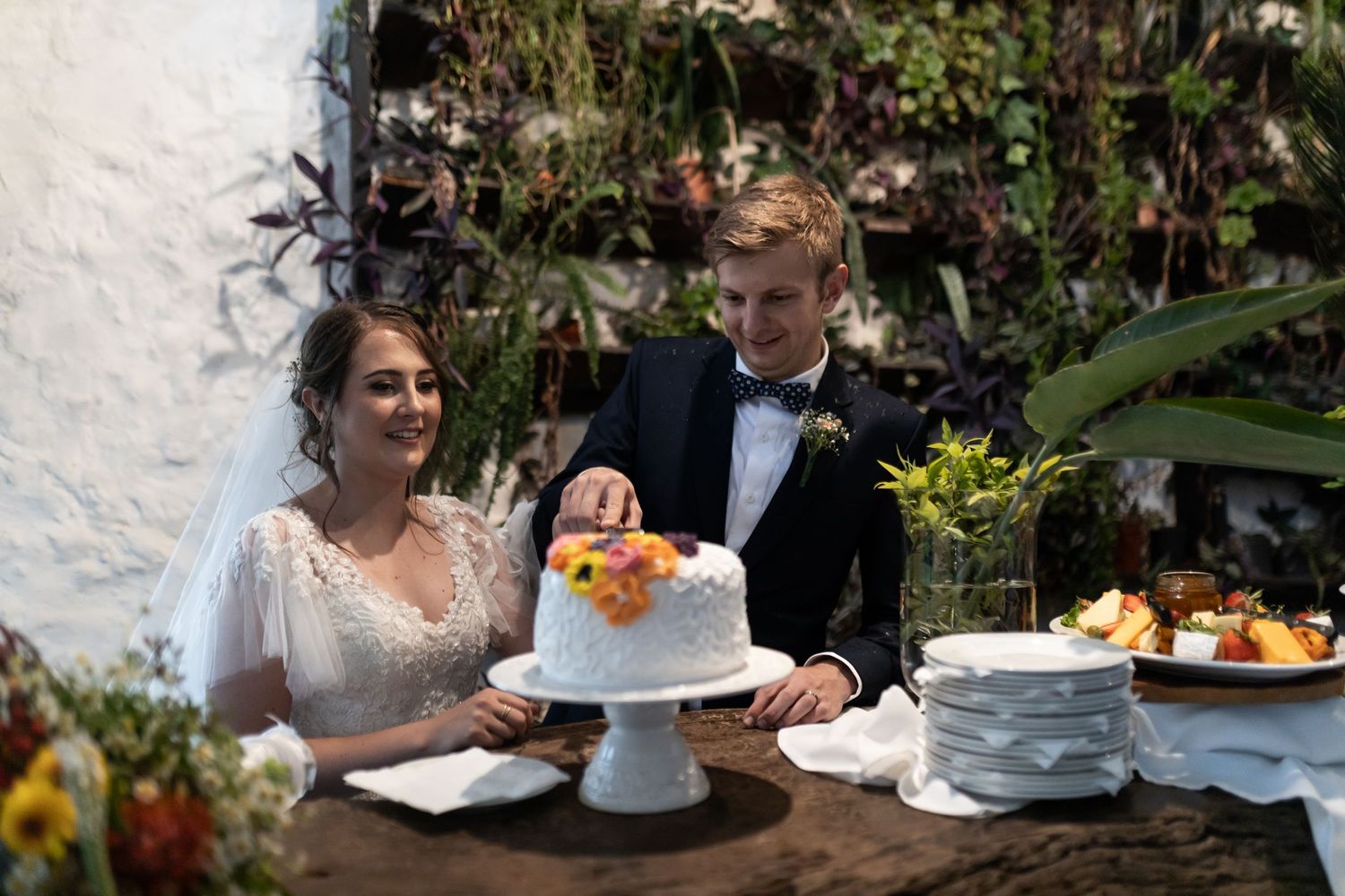 Couple admiring their wedding cake decorated with orange and yellow flowers on a white cake stand.