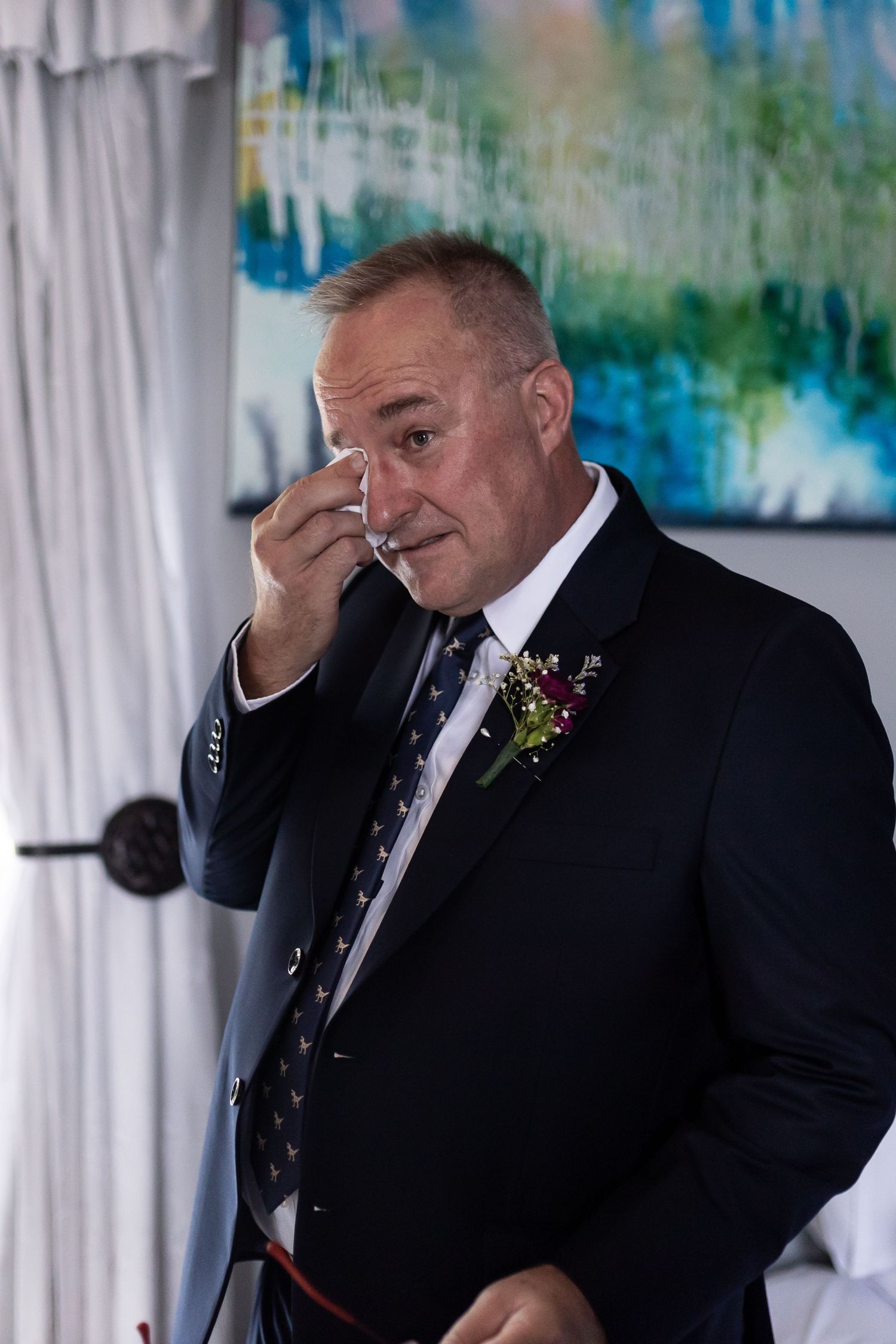 An emotional moment captured during a wedding ceremony with a blue abstract painting in background.