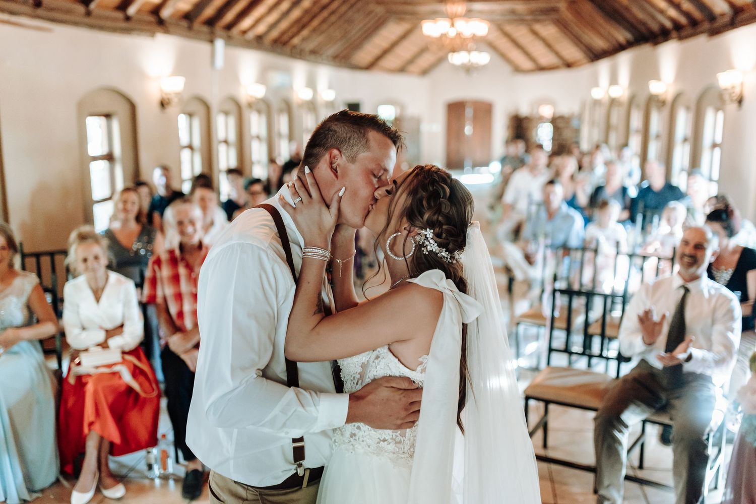 Romantic wedding kiss between couple in rustic venue with exposed wooden beams.