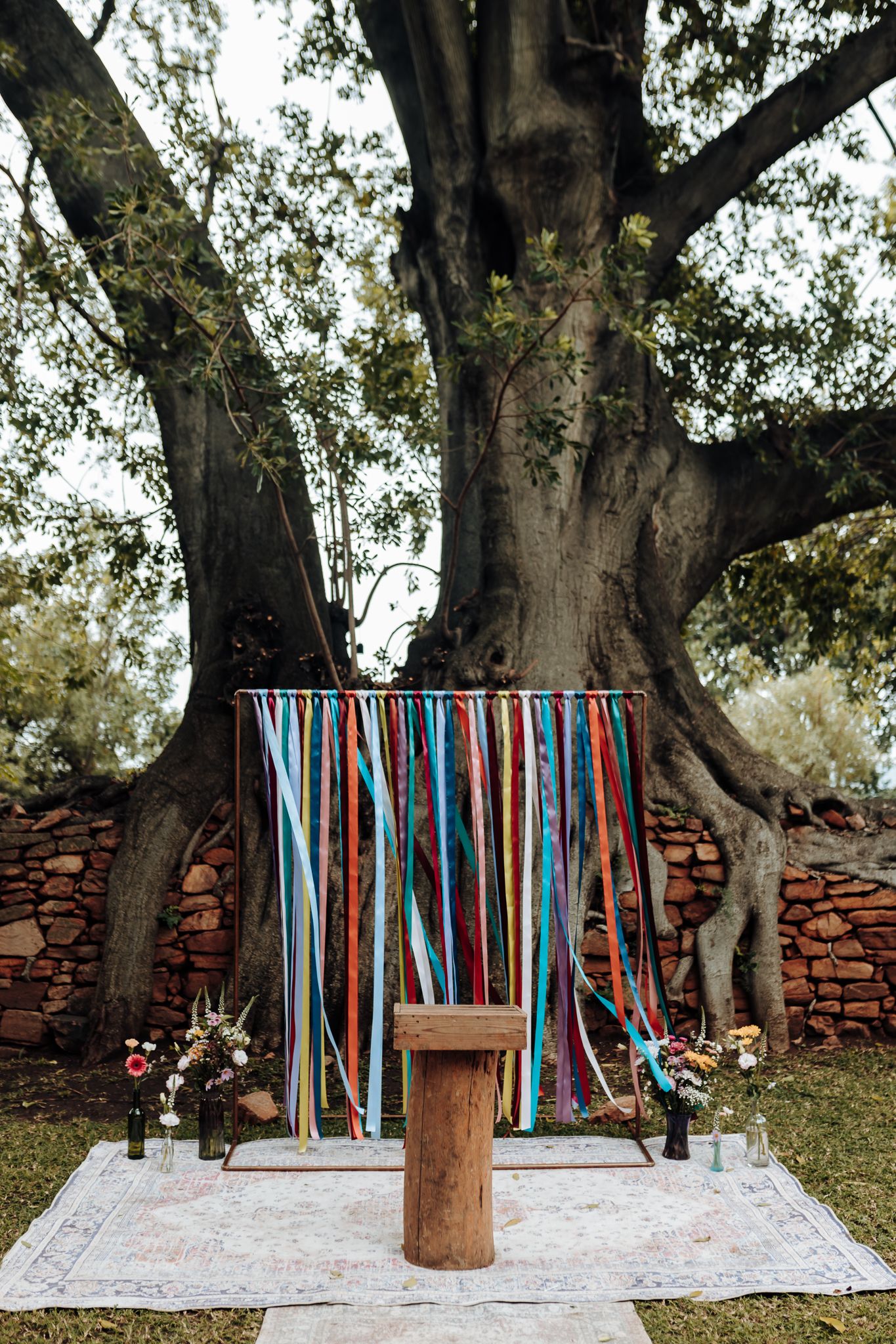 A rustic wedding altar setup with colorful ribbon streamers against a large tree backdrop.