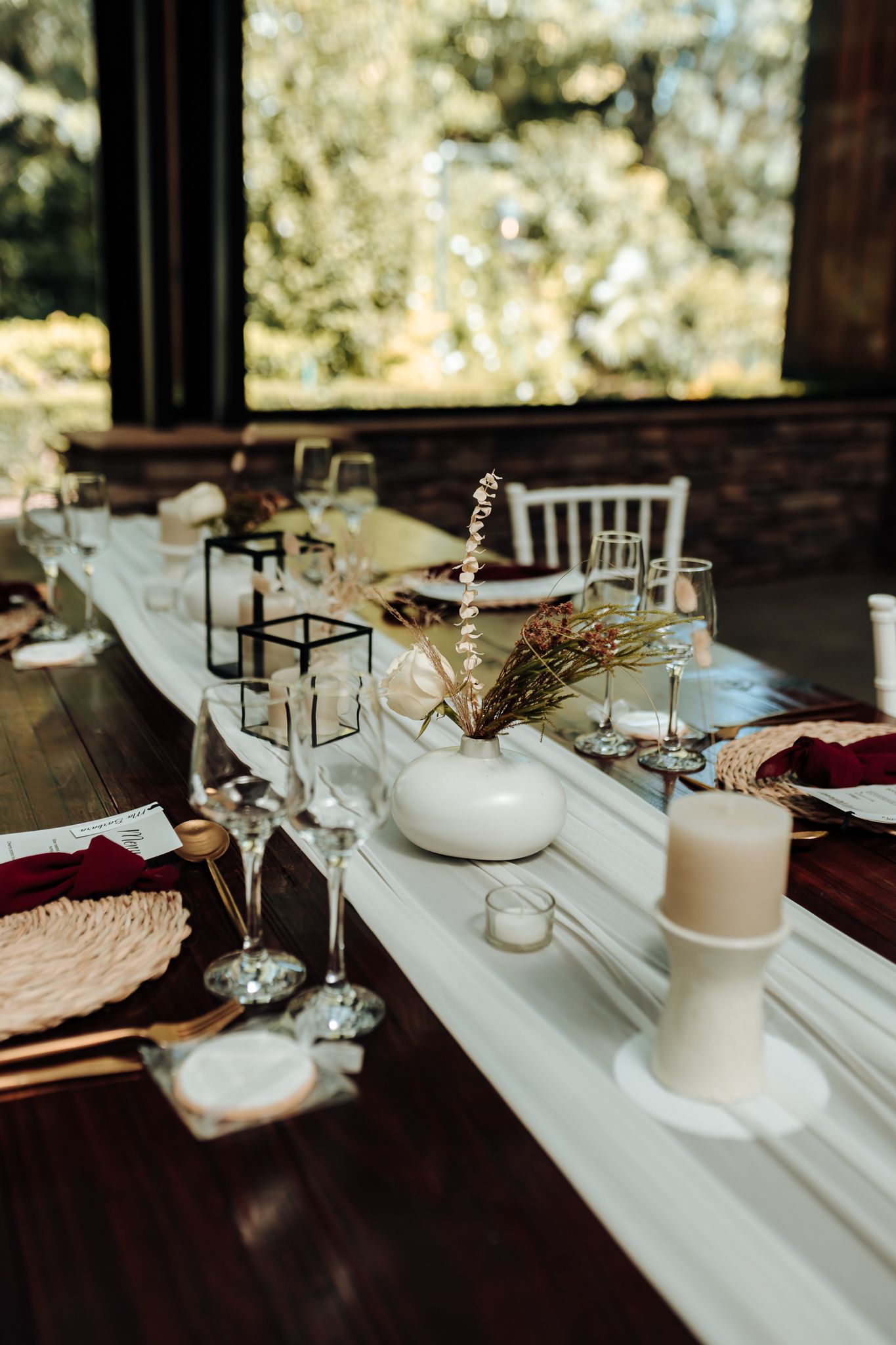Elegant table setting with white runner, candles and dried floral centerpieces for wedding reception.