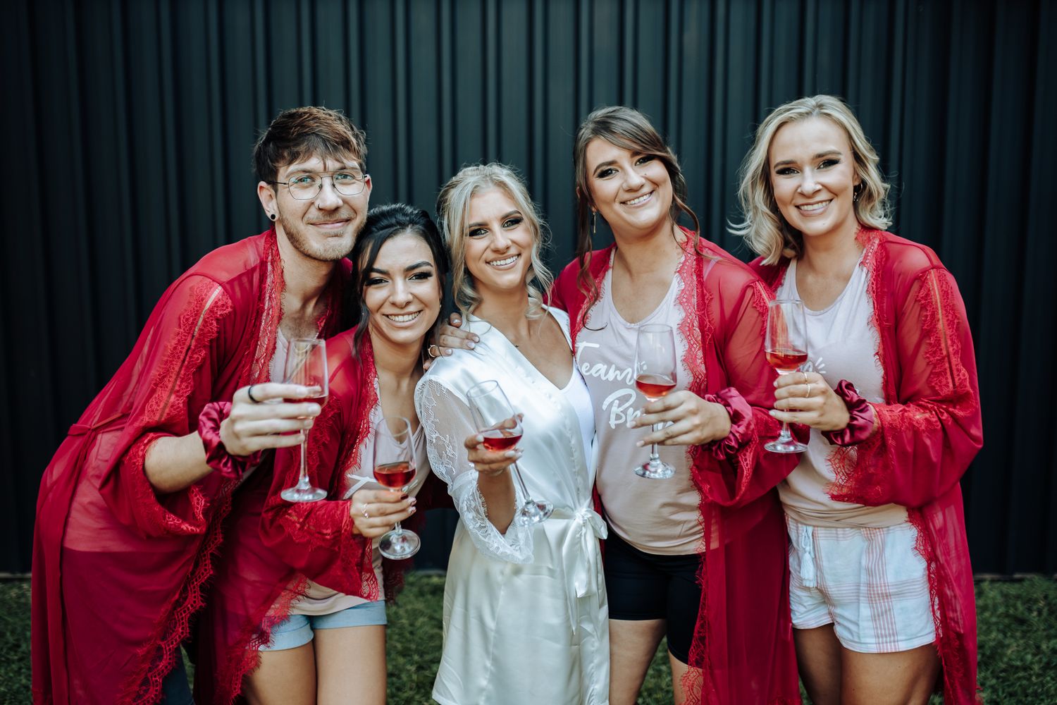Wedding party holding champagne glasses while wearing matching red robes.