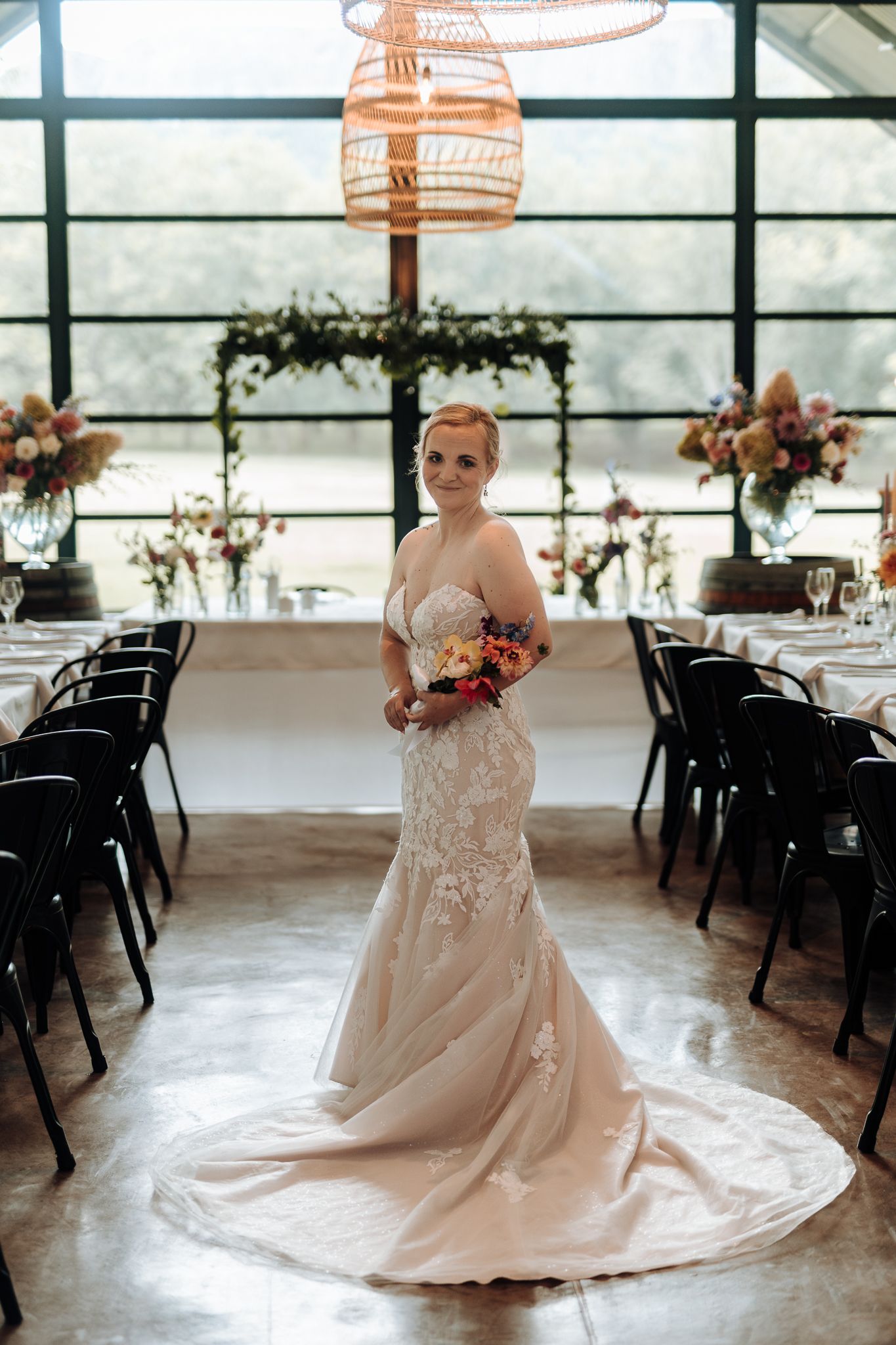 Elegant bride in fitted lace wedding gown poses in modern reception venue with geometric windows and hanging lights.