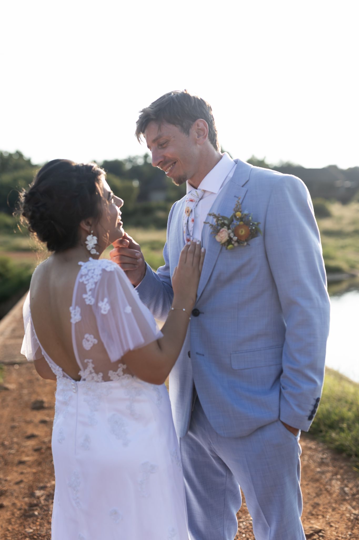 Wedding couple shares joyful moment in pale blue suit and white lace dress outdoors.