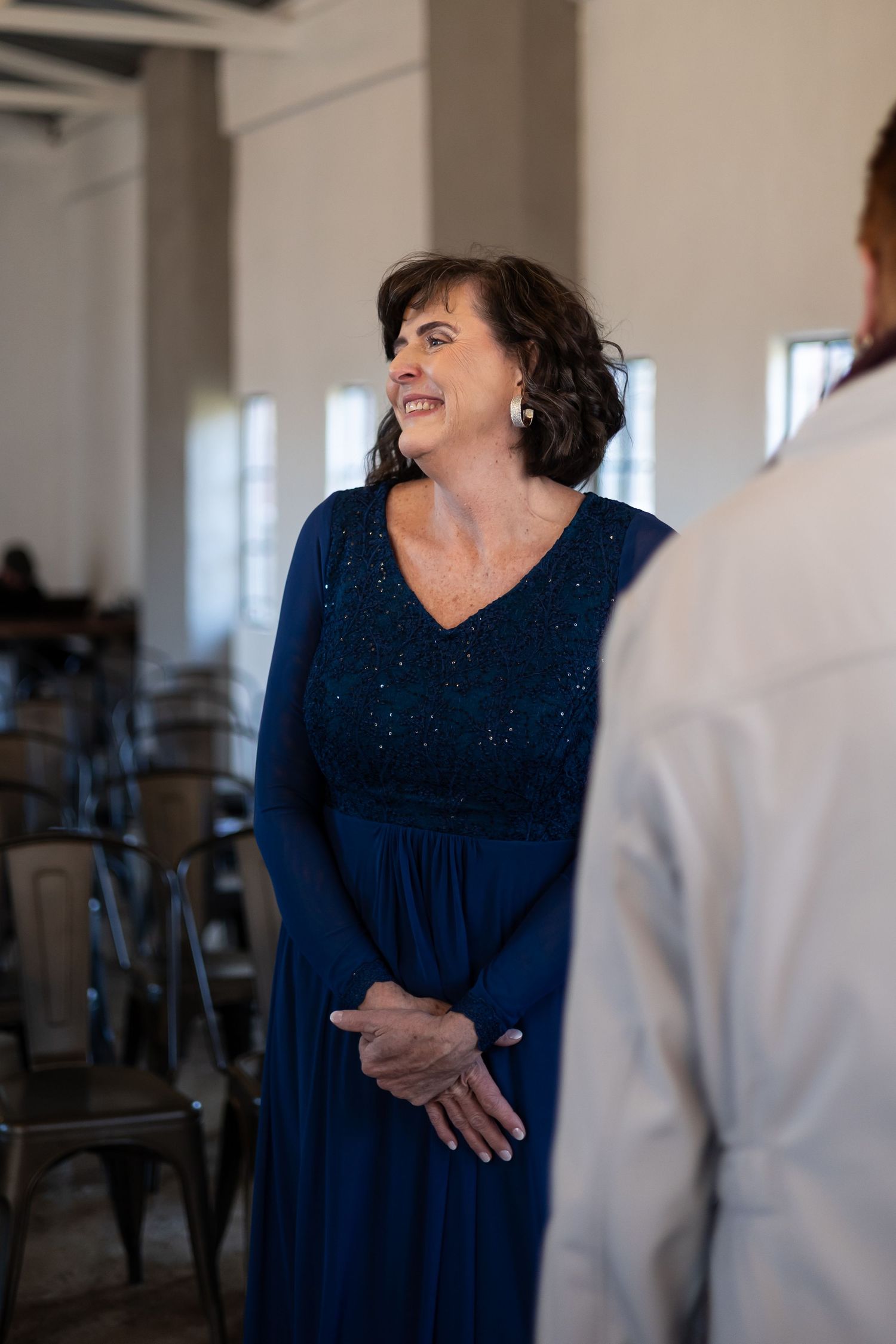 Person wearing a dark navy blue flowing dress is animated in conversation while standing indoors.
