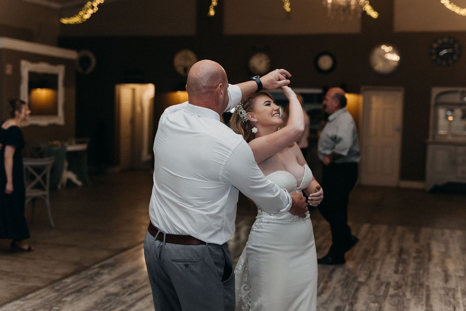 Couple dancing together at wedding reception with warm lighting and wooden floors.