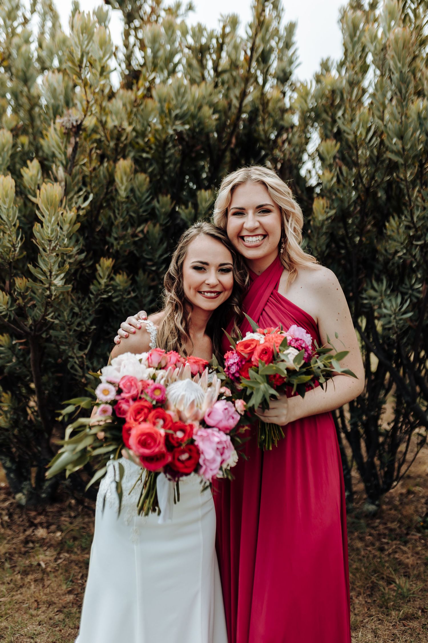 Candid portrait of bride and bridesmaid laughing together while holding floral bouquets.