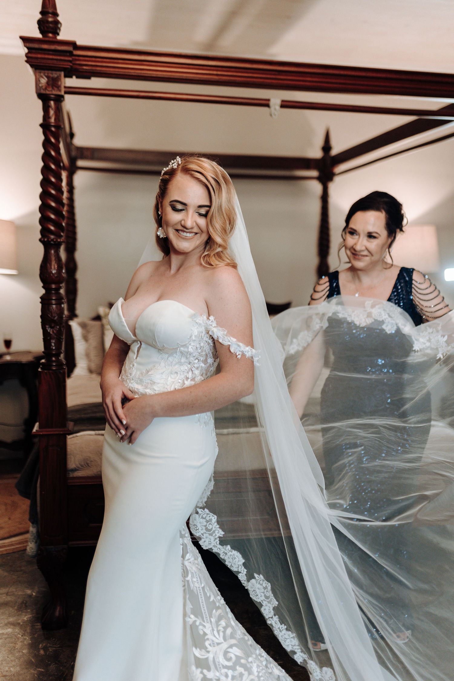 Bride and bridesmaid arranging flowing cathedral veil in natural window light.