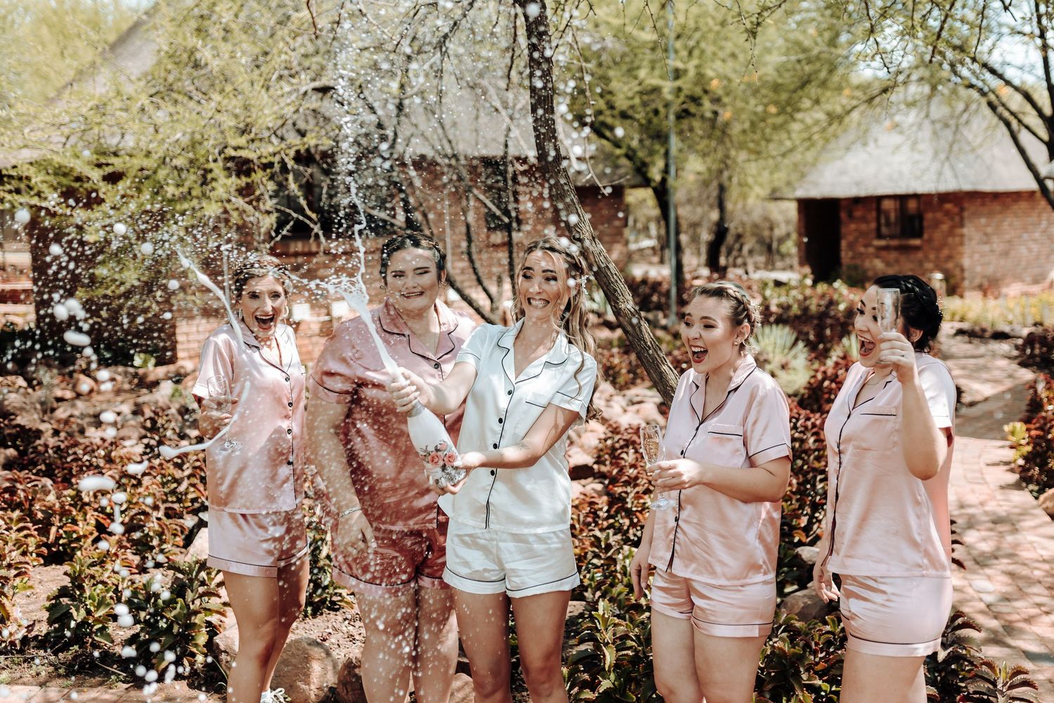 Friends in matching loungewear toss confetti while celebrating in an outdoor garden setting.