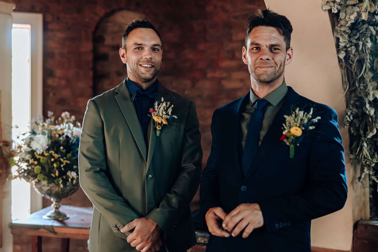 Two people in elegant suits with floral boutonnieres at wedding ceremony.