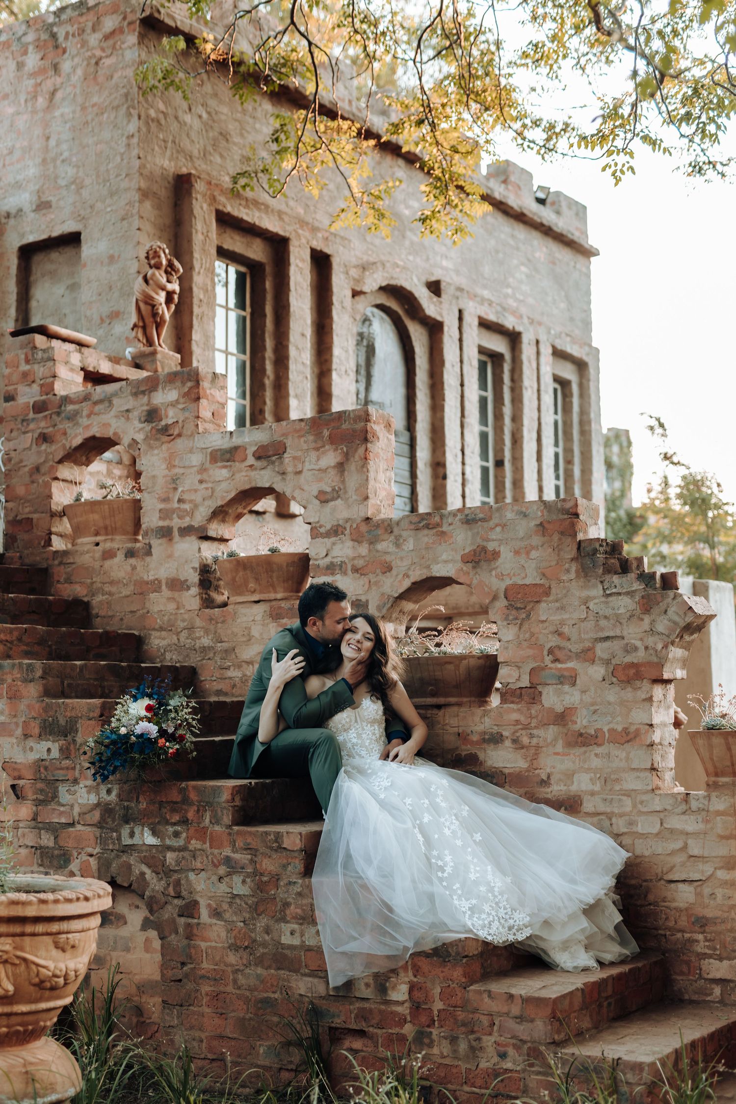 Wedding couple posing on historic stone steps against a weathered brick building facade.