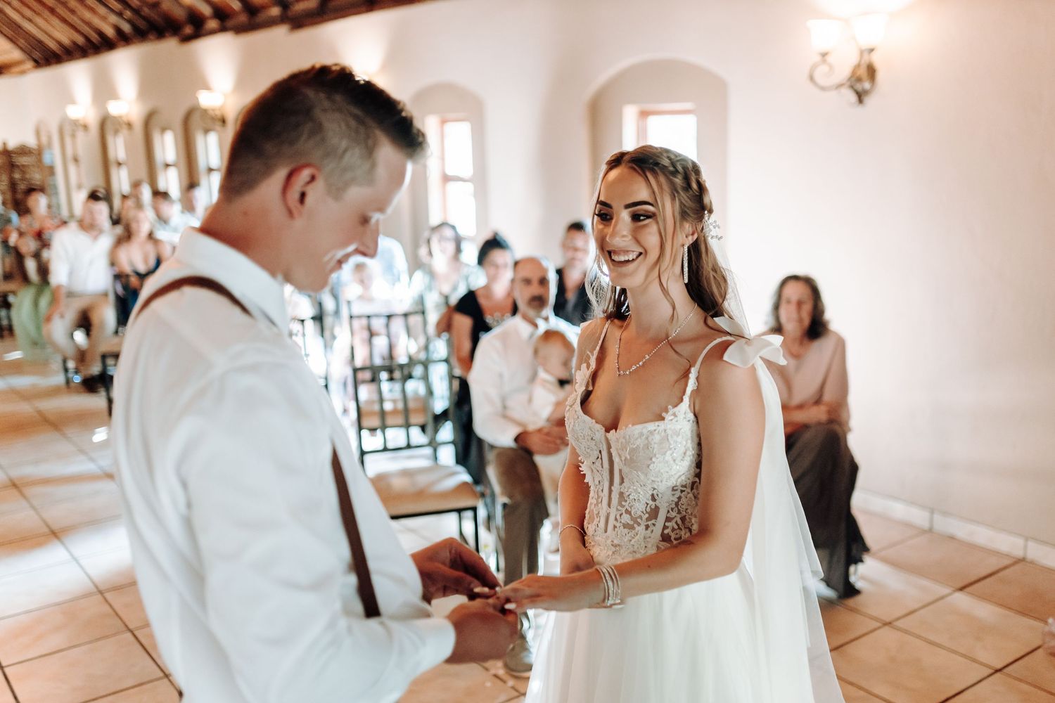 Couple exchanges rings during wedding ceremony in sunlit rustic venue.