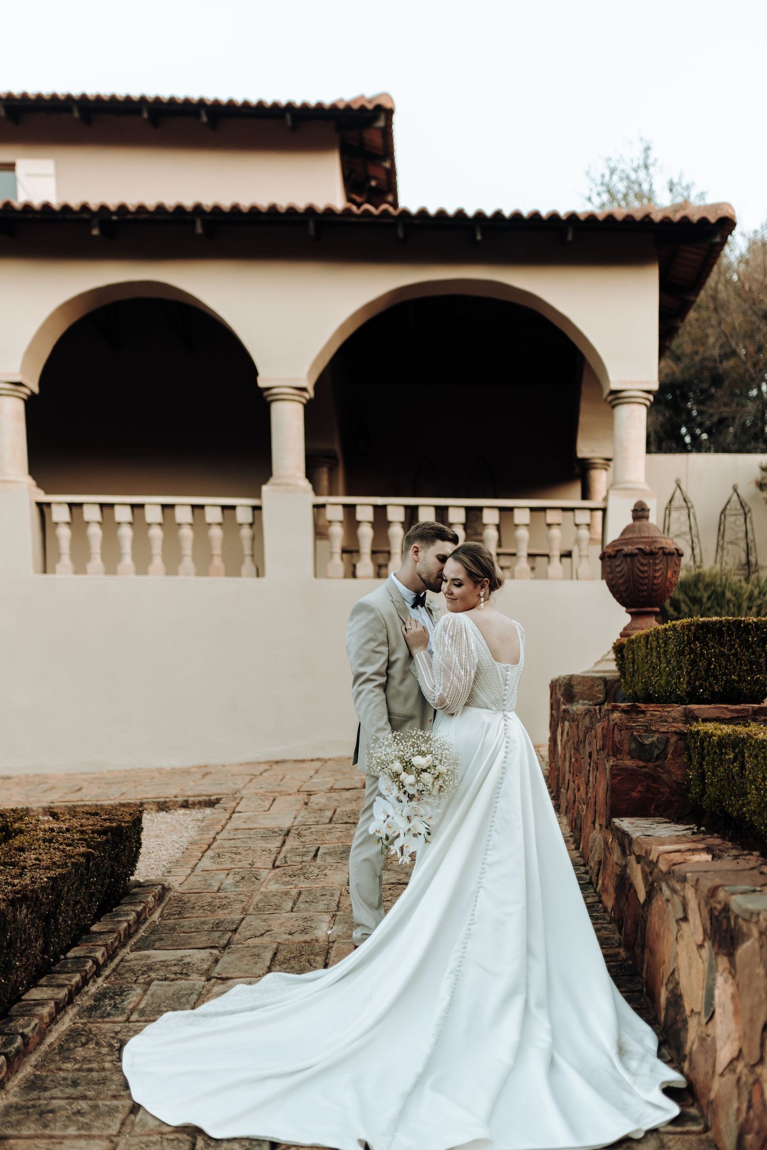 Elegant wedding portrait on stone terrace with Mediterranean architecture backdrop.