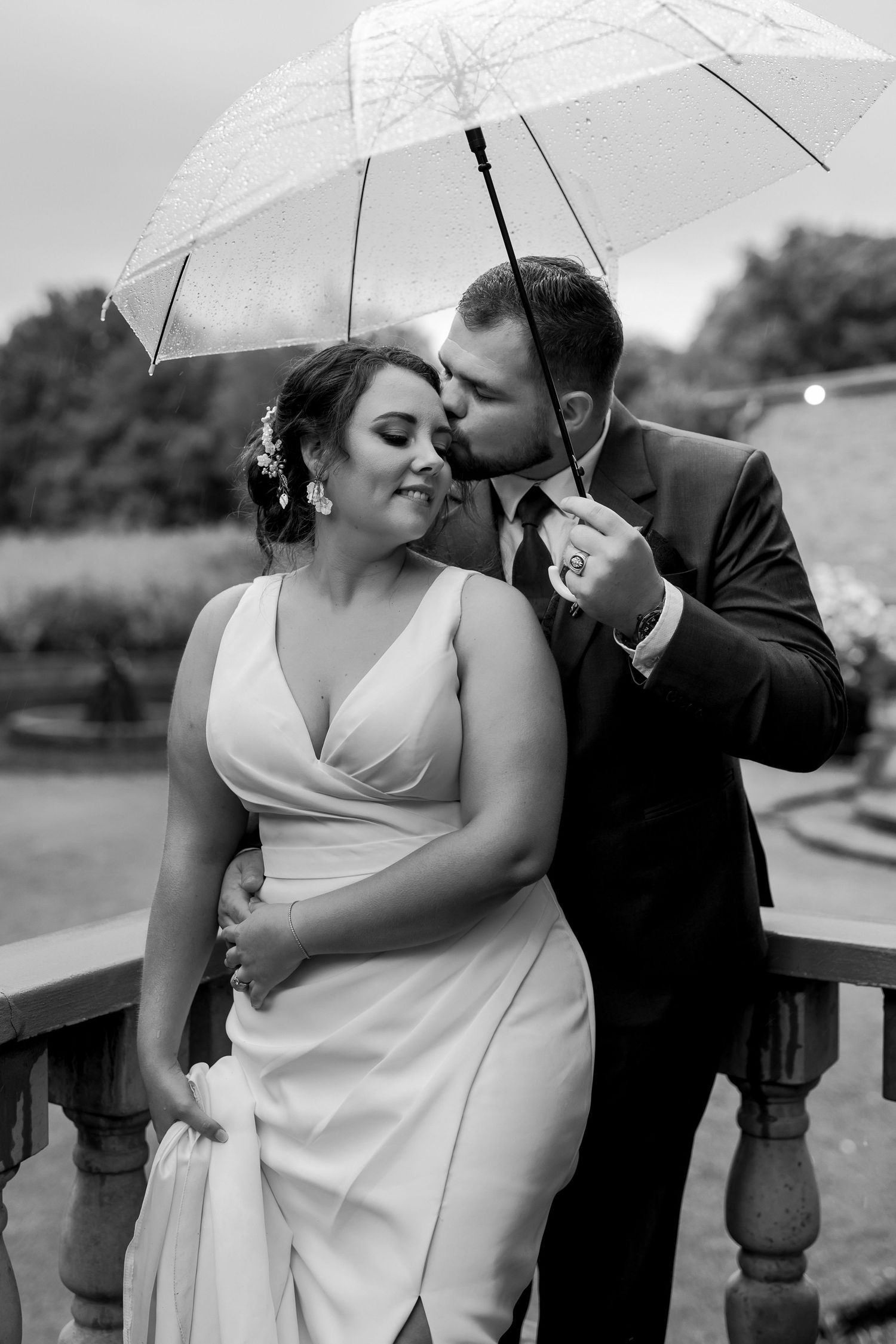Black and white portrait of couple sharing tender moment under white umbrella.