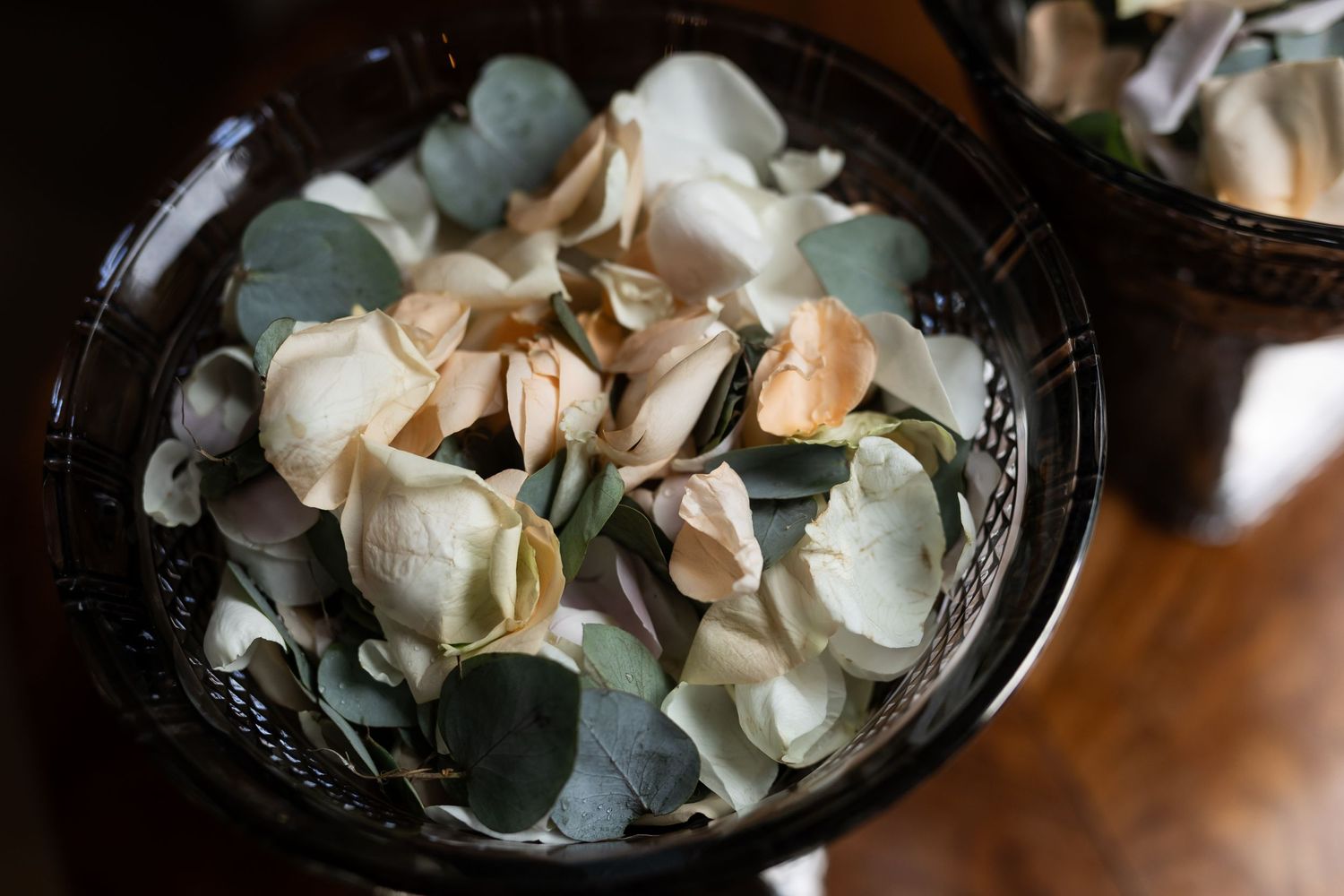 Delicate pale petals and eucalyptus leaves arranged in dark vintage bowl.