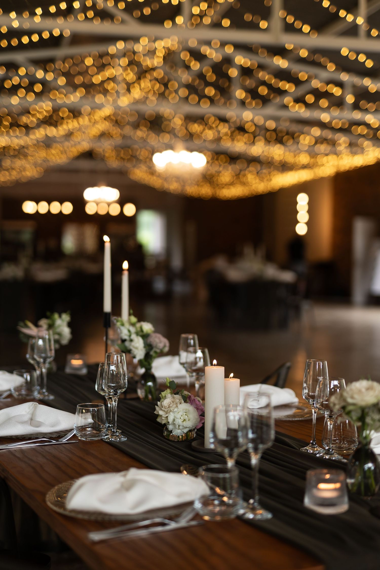 Romantic table setting with candles and floral centerpieces under glowing string light canopy.