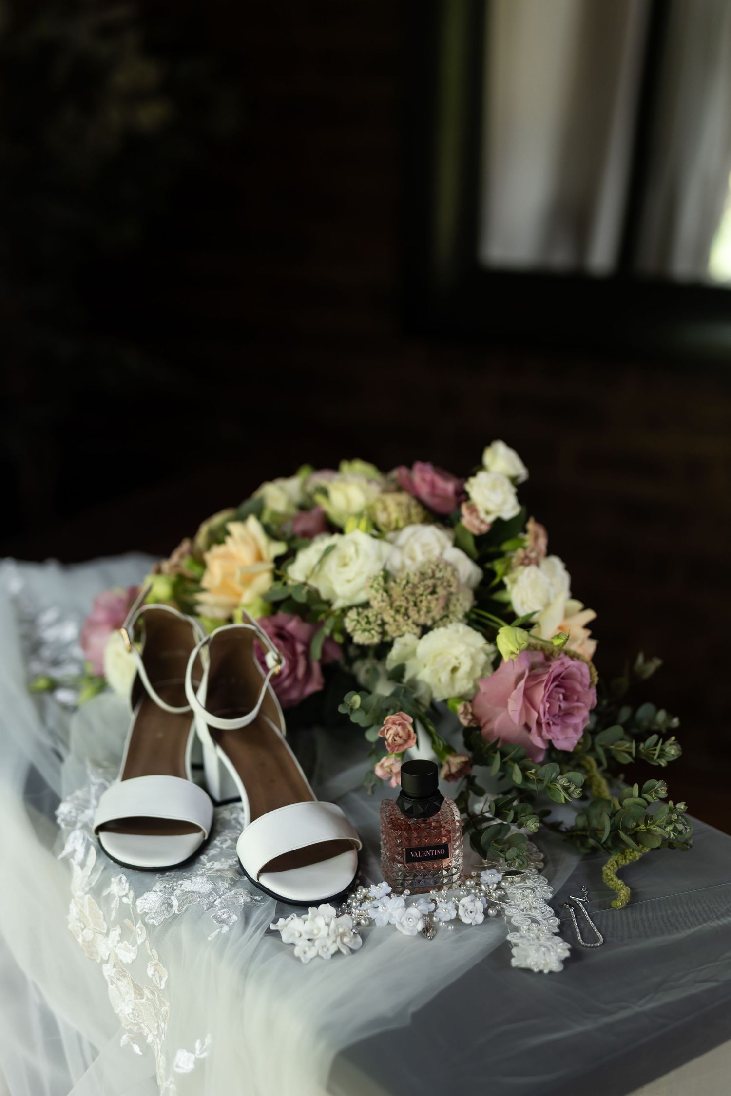 Wedding details featuring white heels and delicate floral arrangement with roses and greenery.