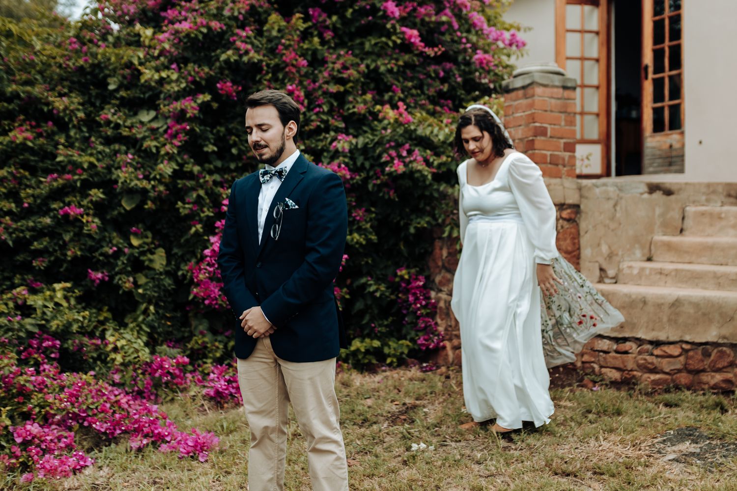 A couple shares a first look moment in front of vibrant pink flowers and stone steps on their wedding day.