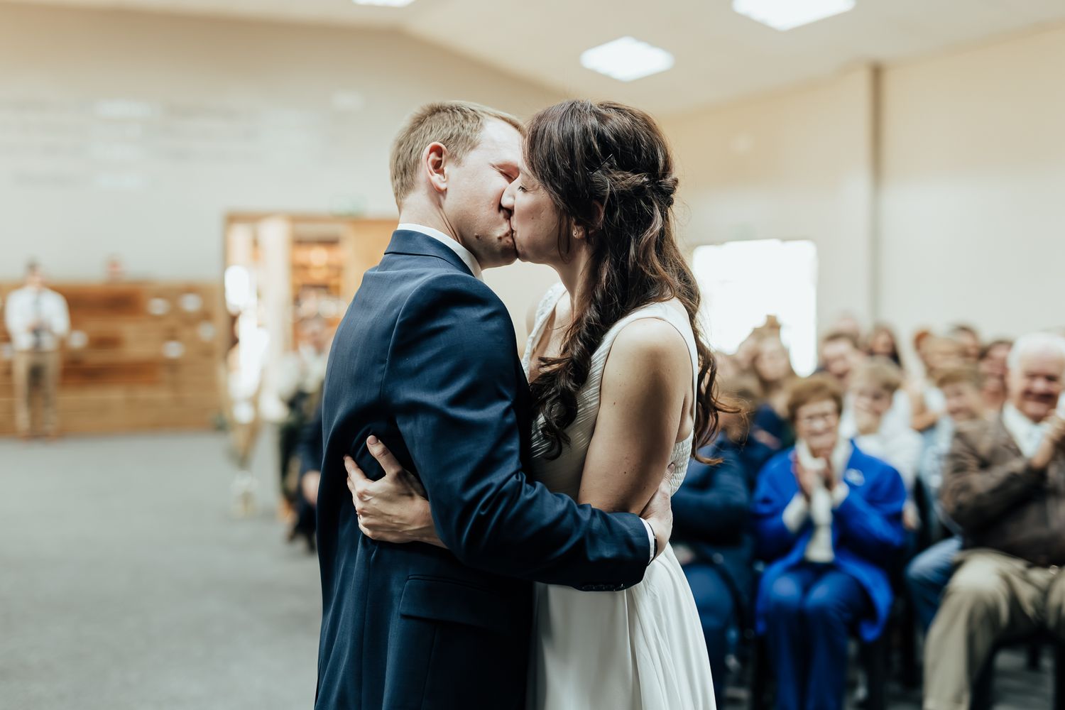 Guests celebrate during an indoor wedding reception with white ceiling lighting.