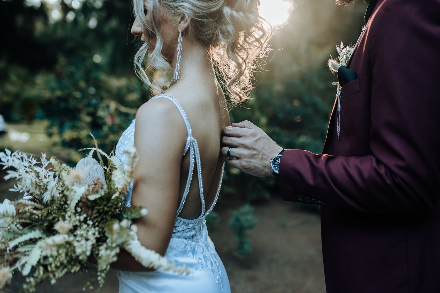 Close up of a wedding dress detail with intricate lace and beading in a garden setting.
