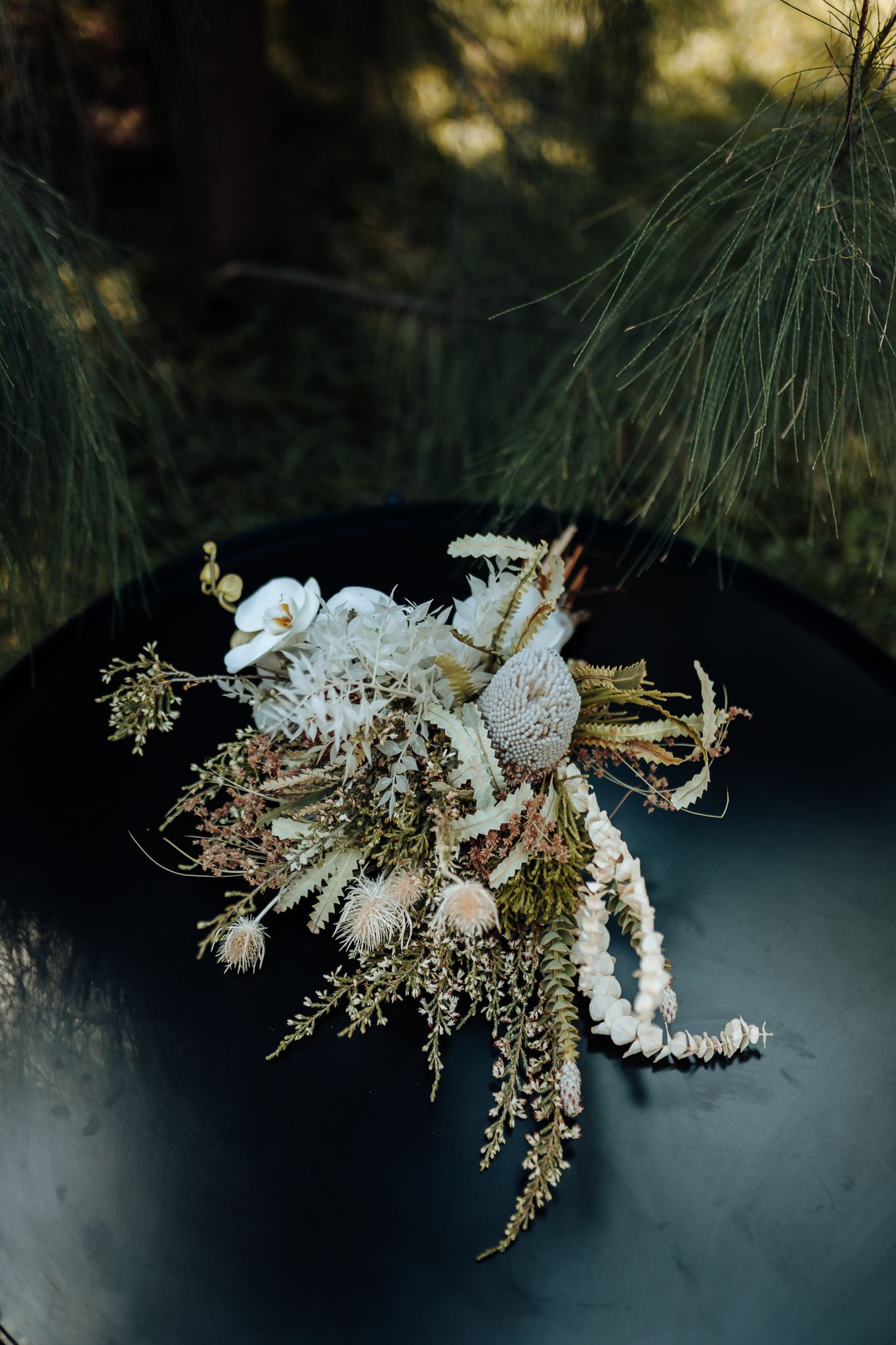 Artistic wedding bouquet with white flowers and dried elements displayed on dark surface.