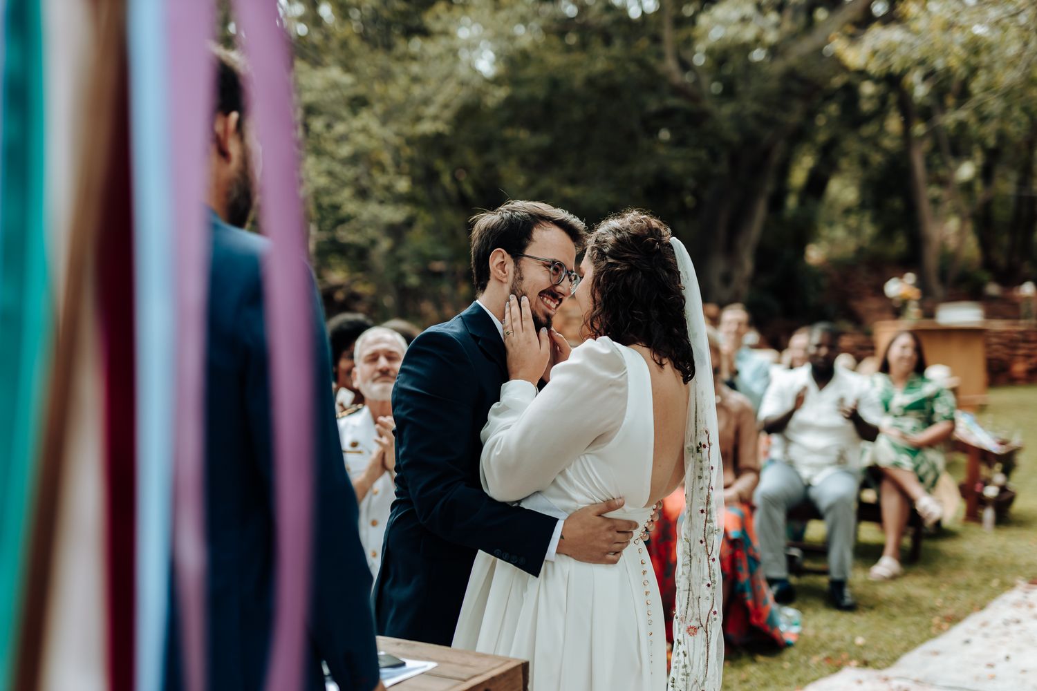 A romantic kiss at an outdoor wedding ceremony with colorful ribbon streamers in the background.